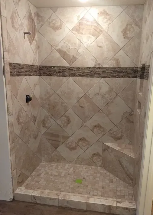 A walk in shower with tile walls and a bench.