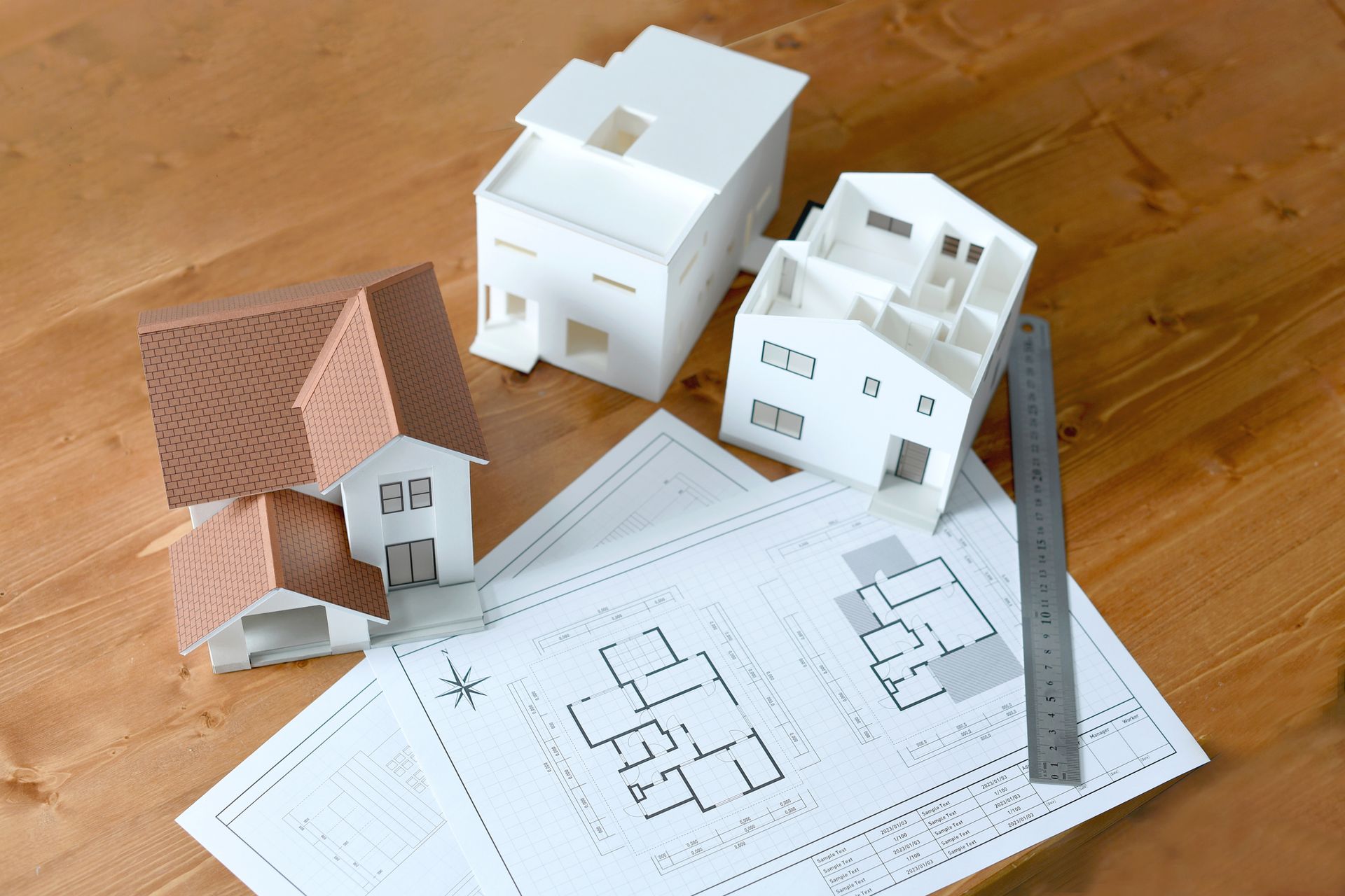 Three model houses are sitting on top of a wooden table next to a ruler.