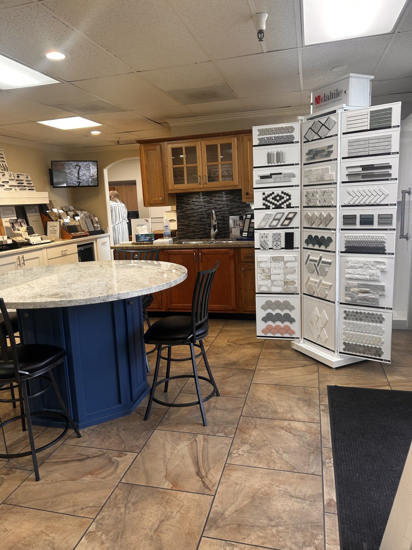 Interior of a showroom with tile displays, a kitchen island with granite countertop, and a person in the background.