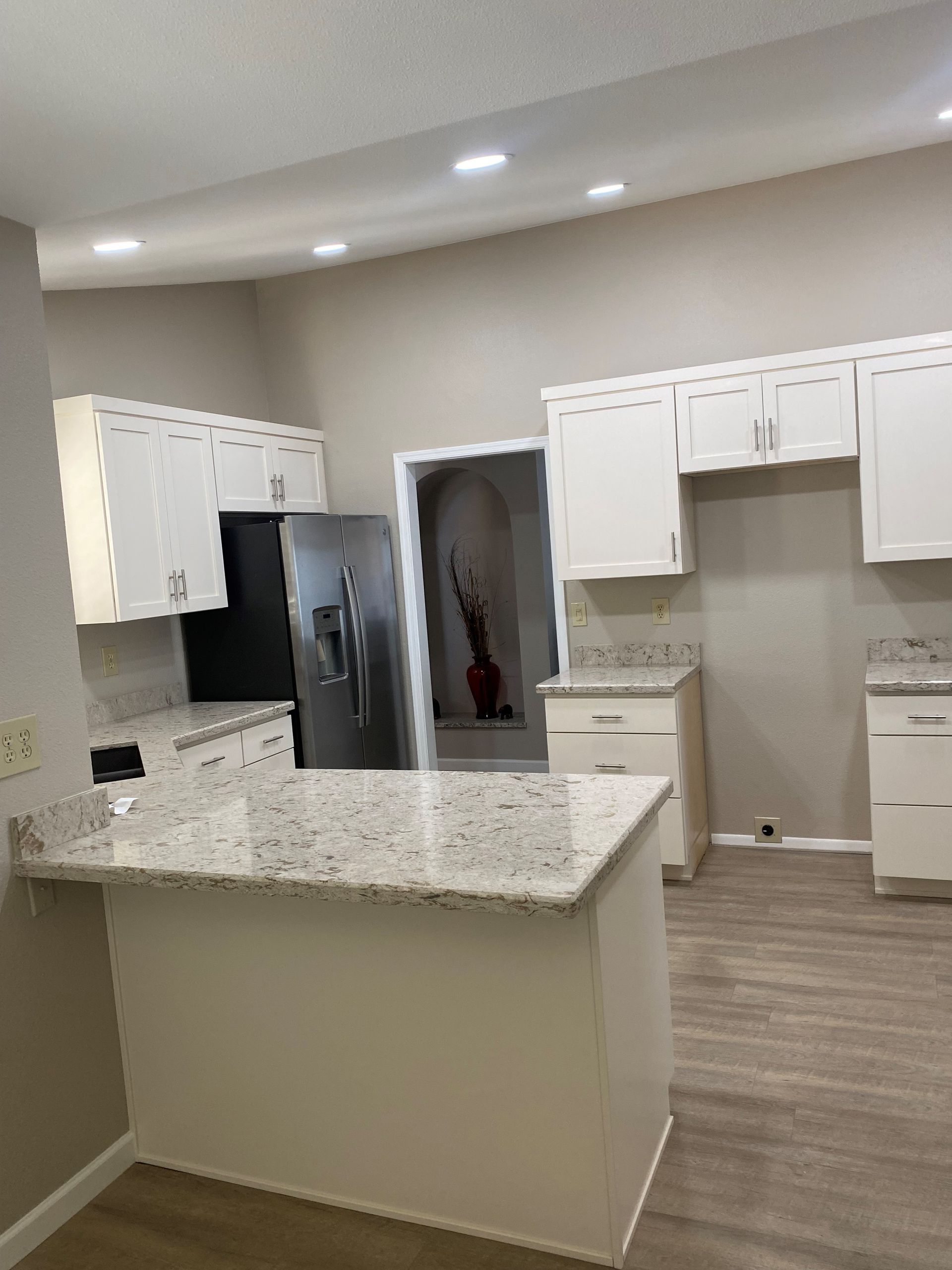 White kitchen with granite countertops and stainless steel refrigerator. Light-colored walls and flooring.