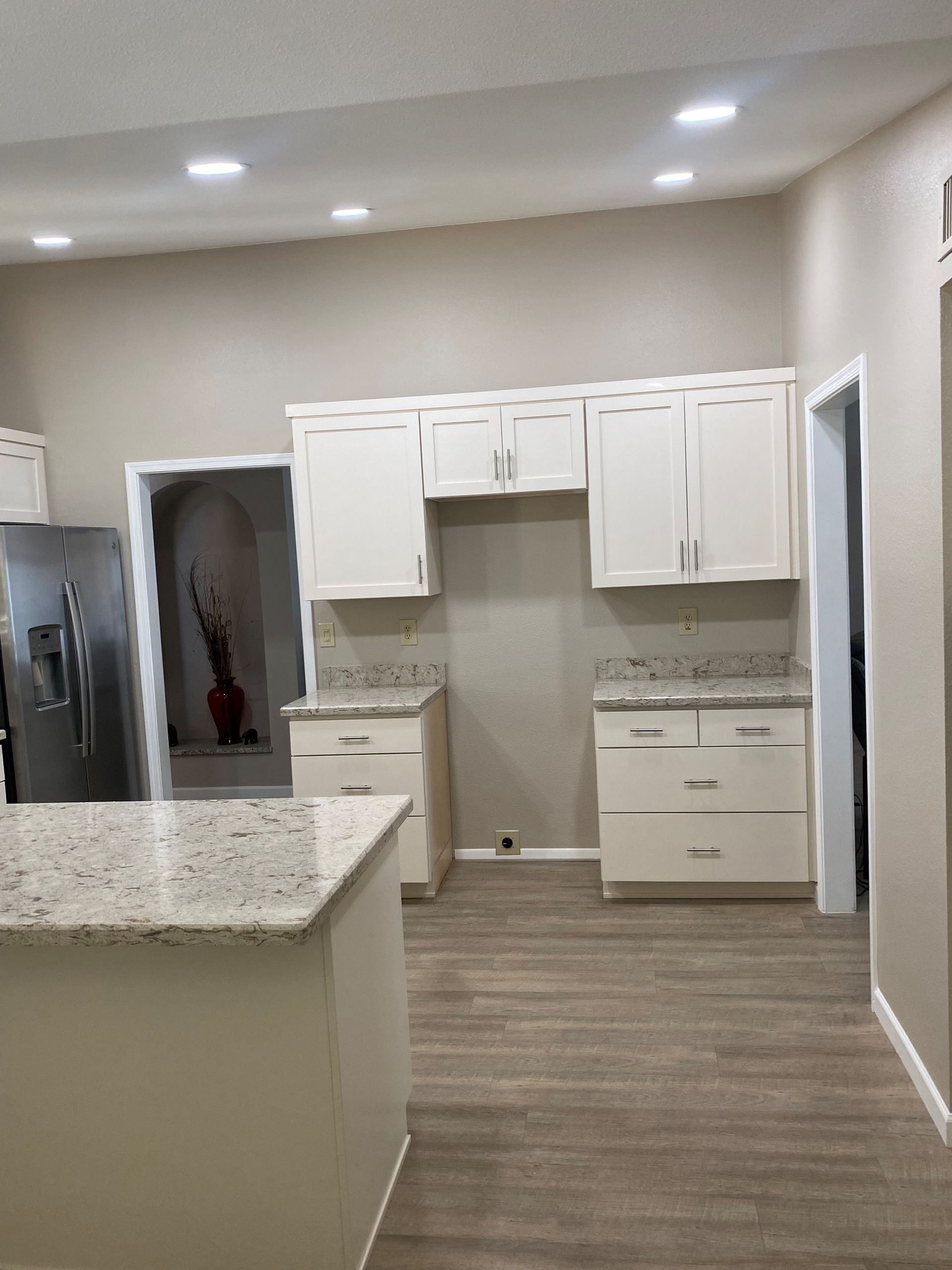 A modern kitchen with white cabinets, granite countertops, and light-colored wood flooring.