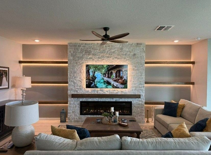 Living room with a stone fireplace, TV, shelves, and couches. Warm lighting.