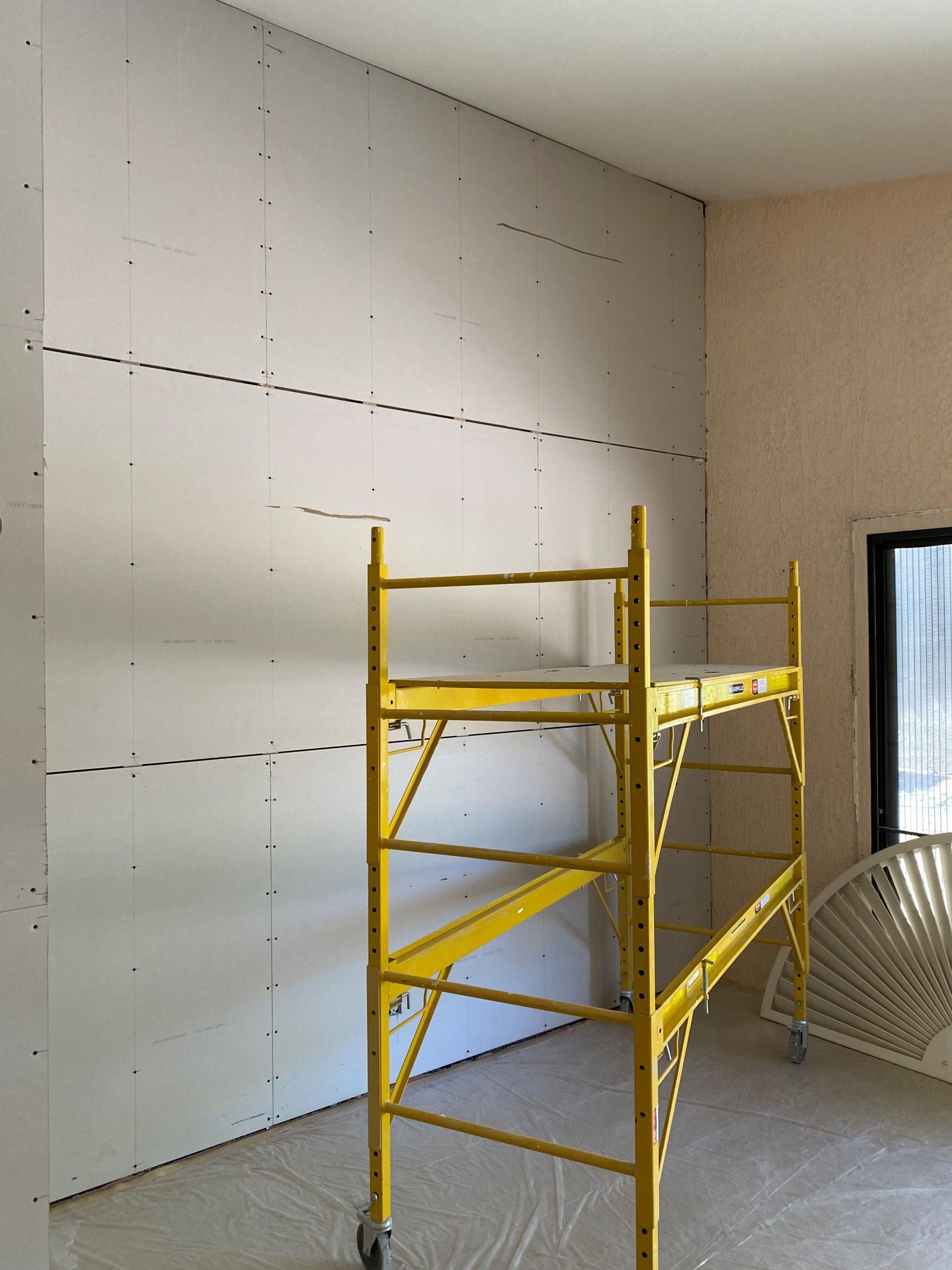 Yellow scaffolding in a room with drywall walls. Construction in progress.