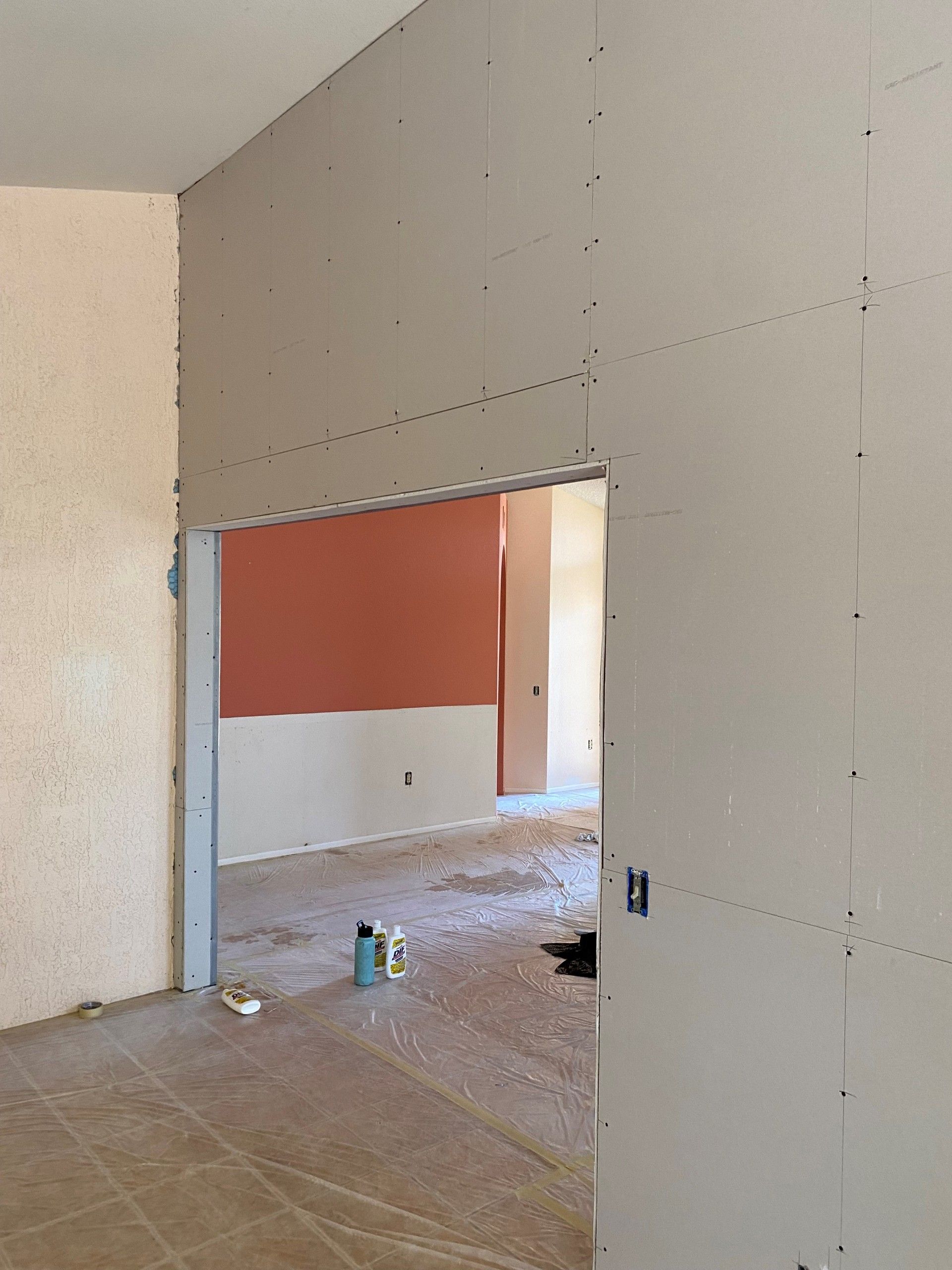 Room with drywall installed, doorway to another room. Walls are off-white and partially painted. Construction site.