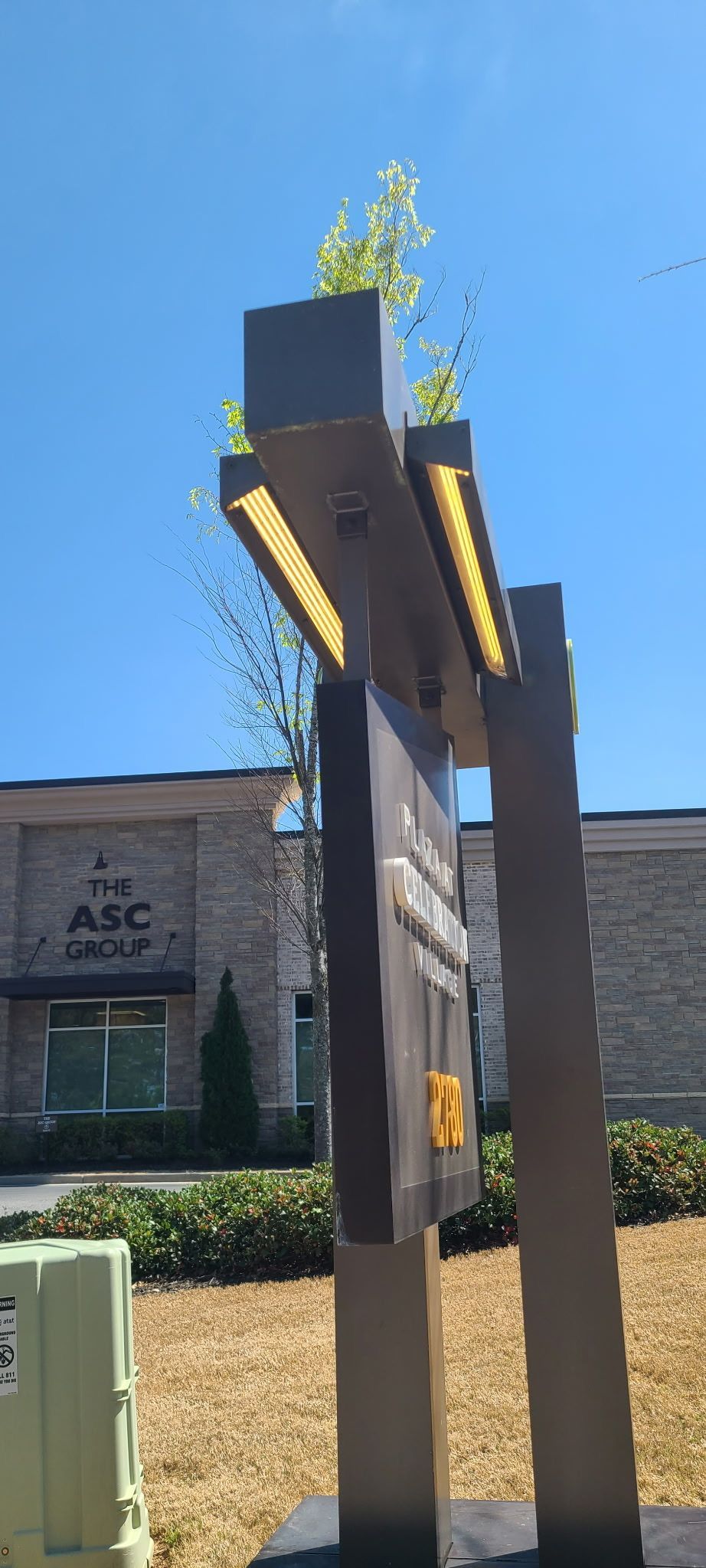 Modern wooden sculpture with green plants on top outside a building under a blue sky