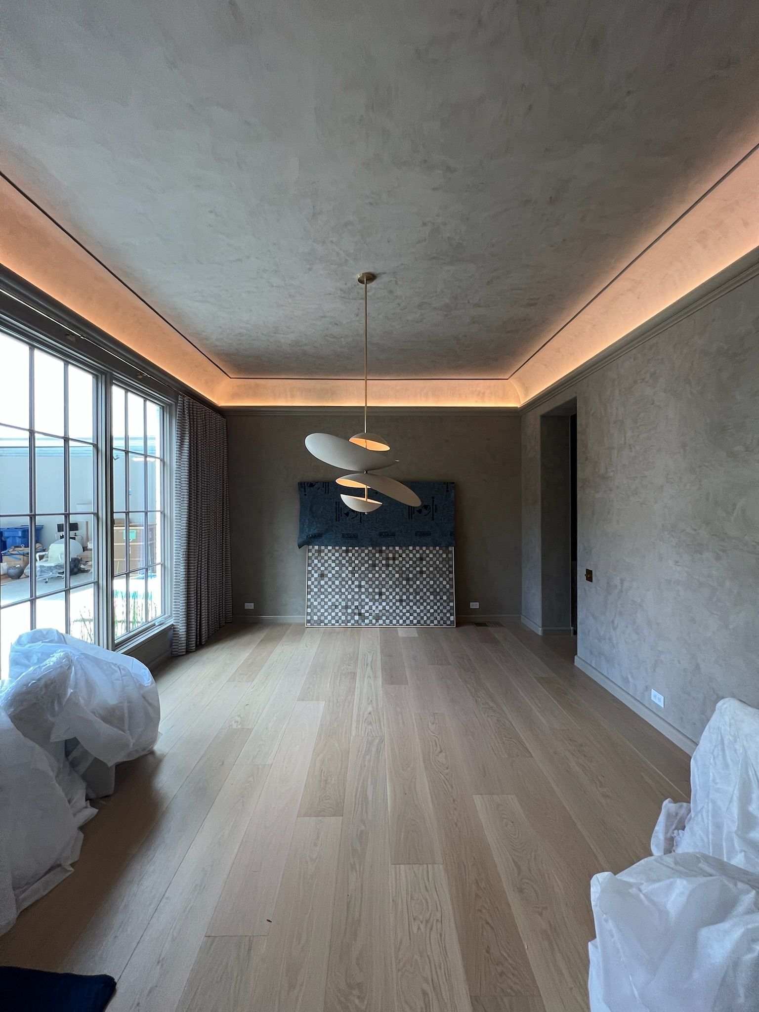Empty modern living room with wood floor, gray walls, recessed lighting, and large windows along the left side