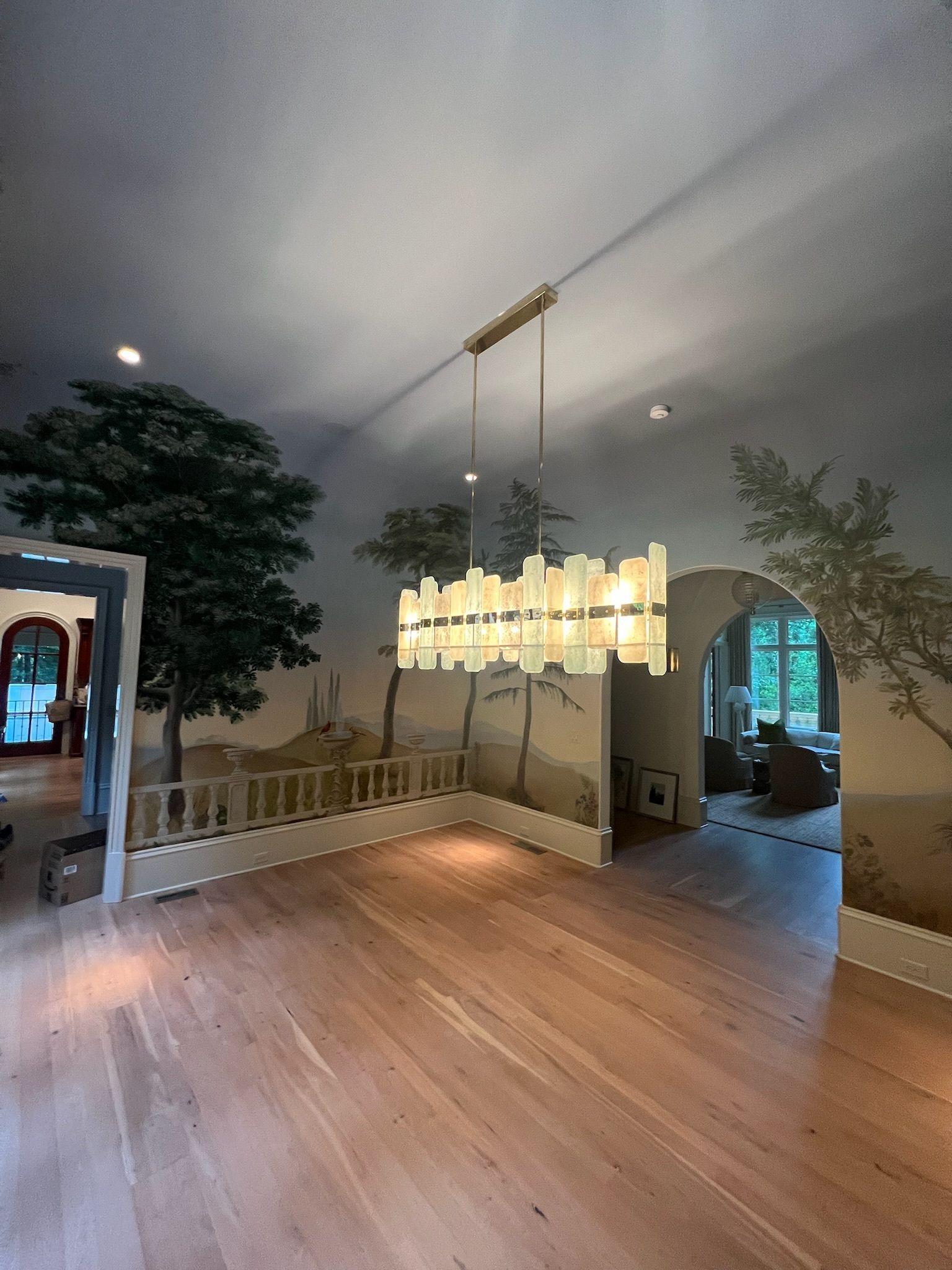 Modern living room with wood floor, chandelier, and wall mural overlooking a balcony and doorway