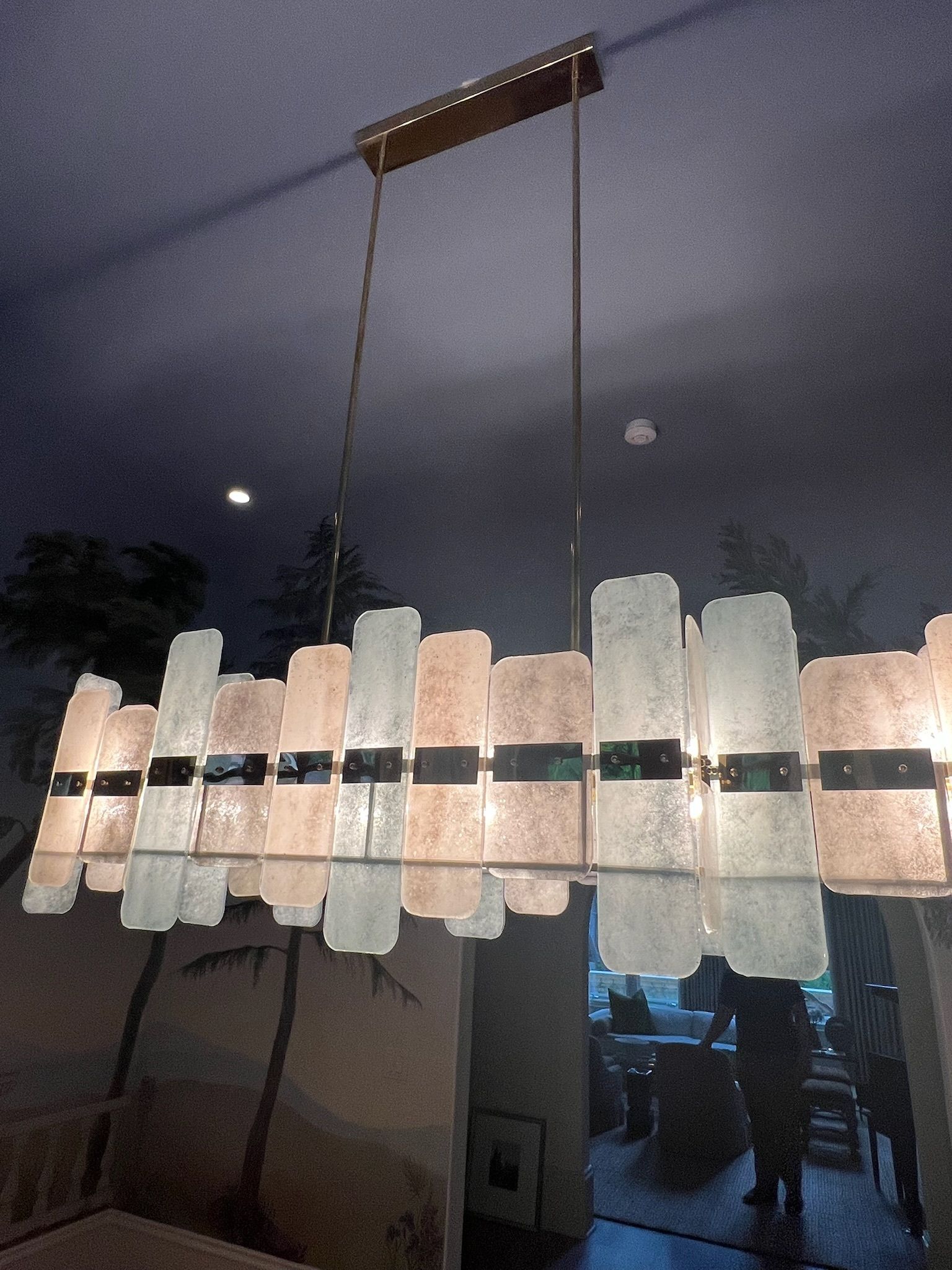 Chandelier with translucent glass panels and black accents hanging indoors against a dim room and window reflection