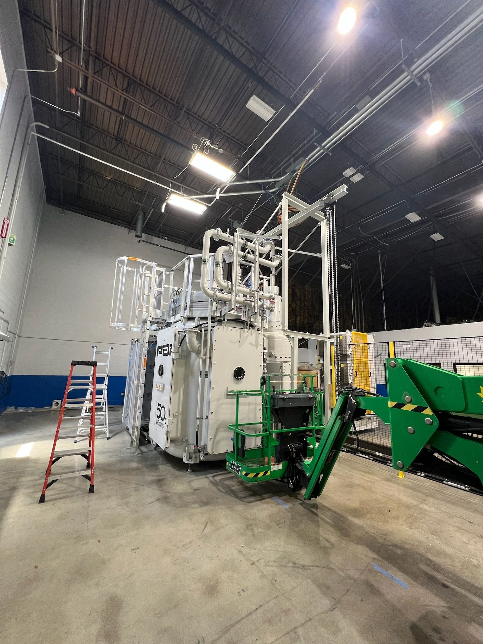 Industrial factory machine with white equipment, green machinery, and a red ladder in a large warehouse.