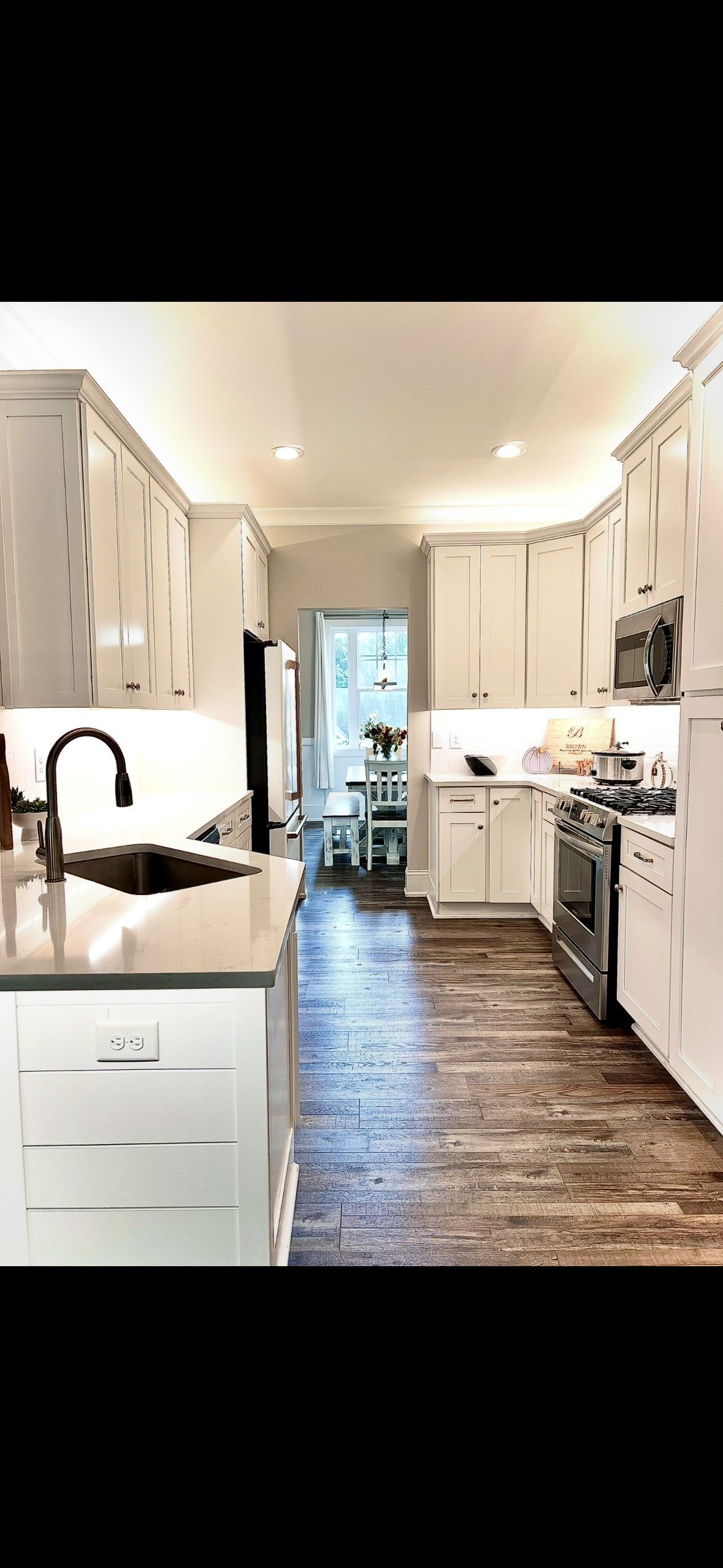 Bright, modern kitchen with white cabinets, dark countertops, and wood flooring, viewed toward a glass door.