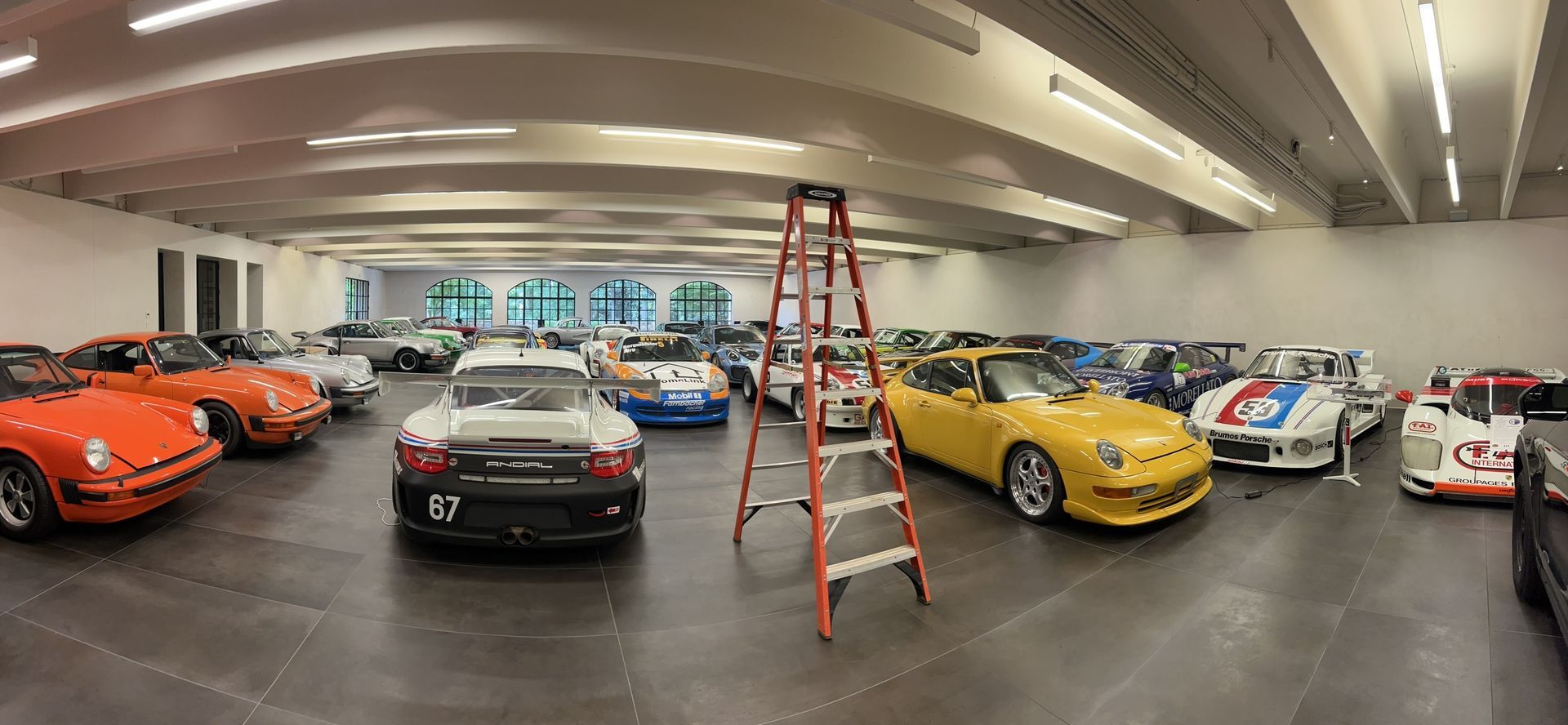 Classic cars displayed indoors, with a red ladder centered between orange, black, yellow, and white vehicles.