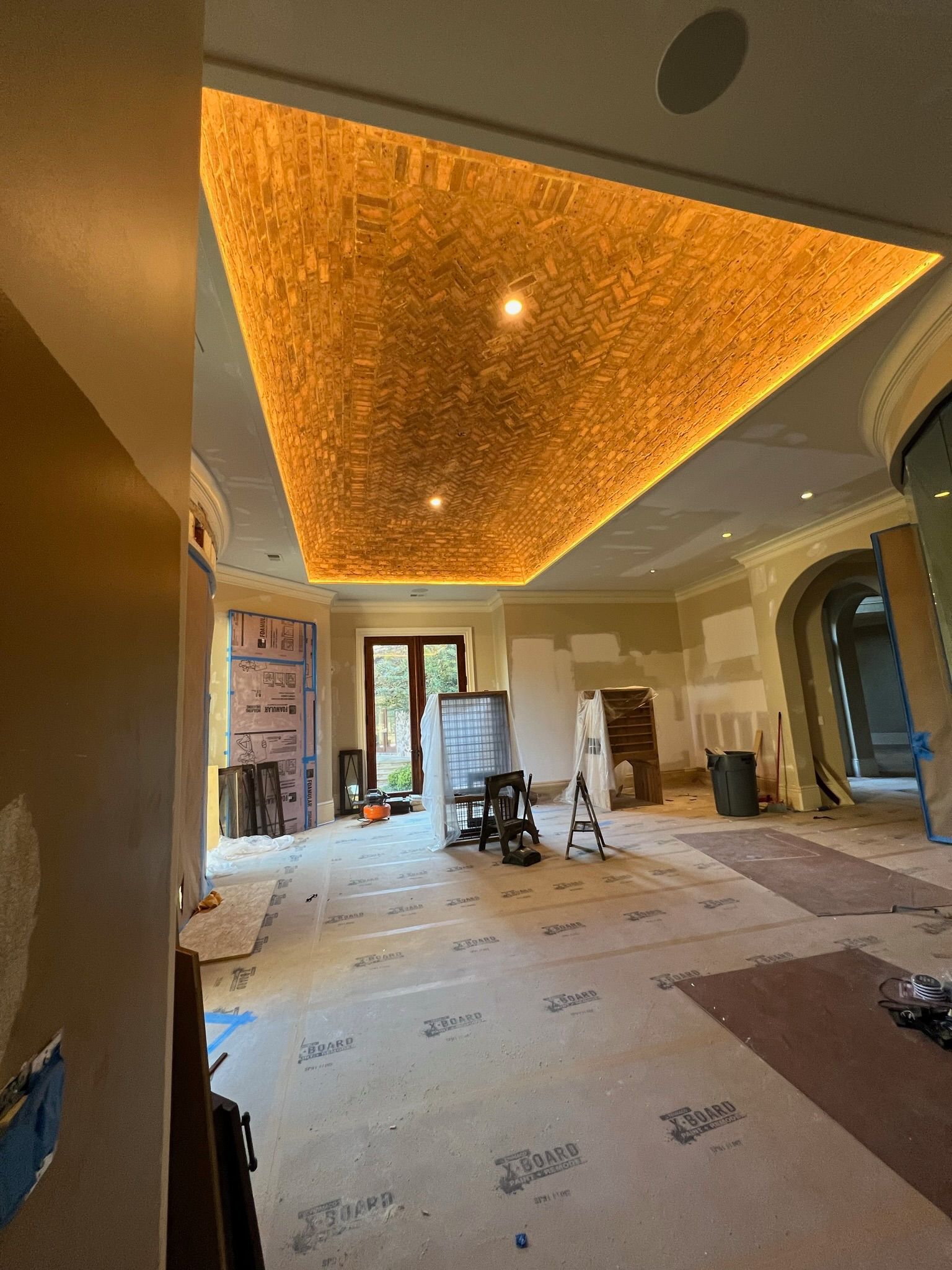 Interior under renovation with lit textured ceiling, bare floor, and construction materials in a room with tall windows.