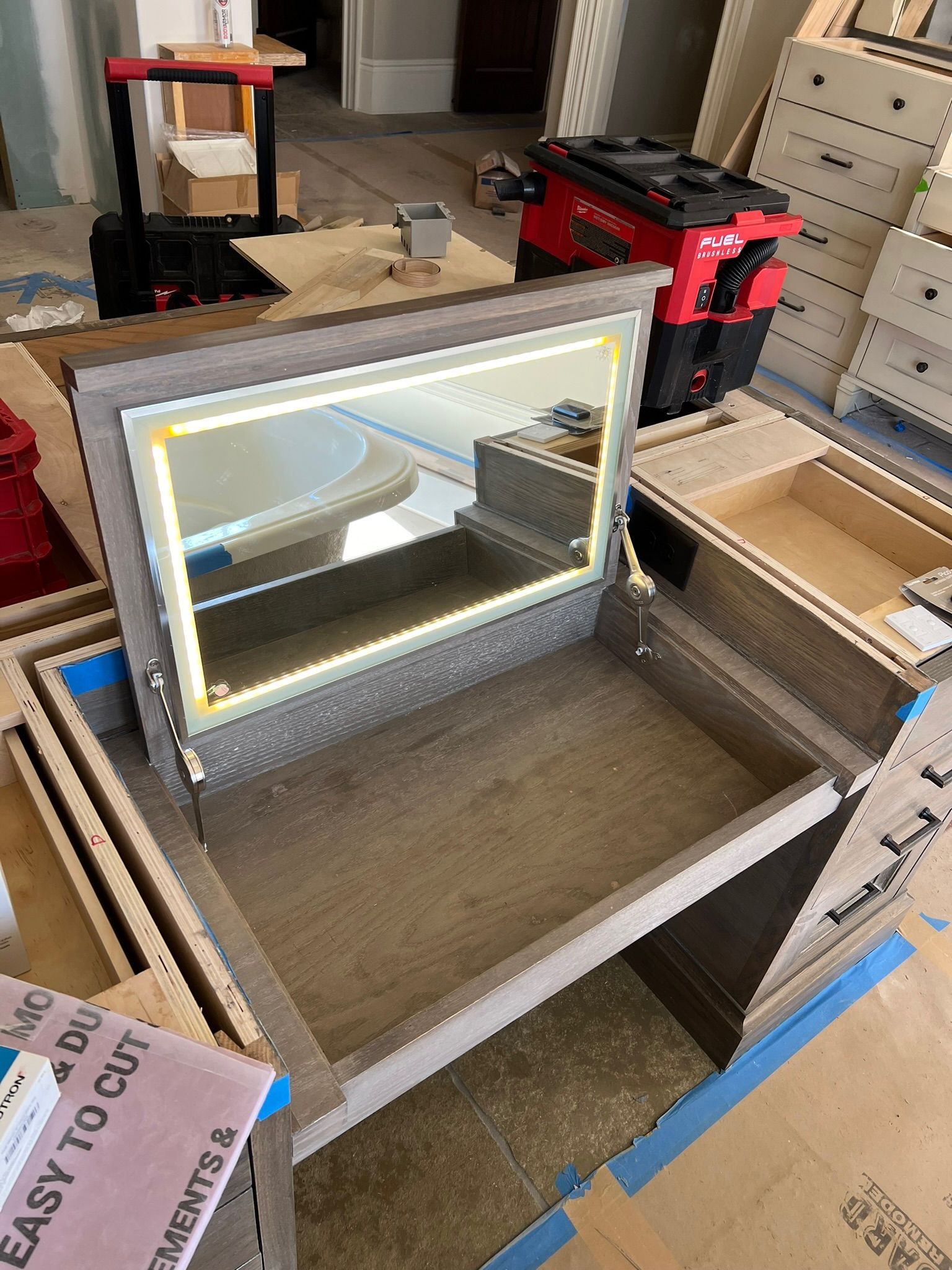 Open drawer with a mirrored panel in a cluttered room, surrounded by tools and cardboard boxes.