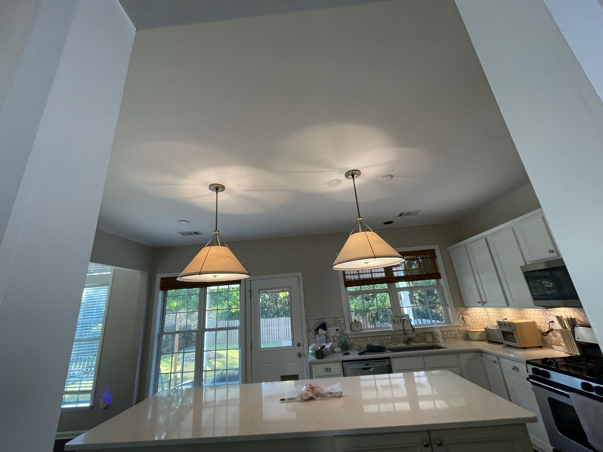 Bright modern kitchen with white island, pendant lights, and large windows overlooking a patio