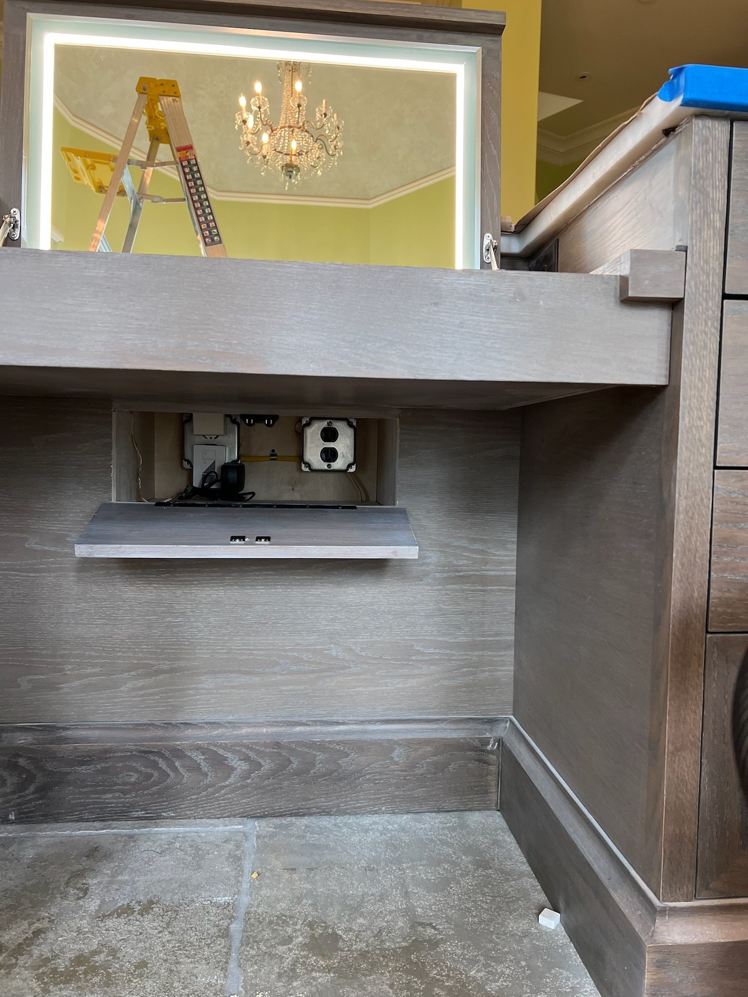 Gray utility cabinet with an electrical outlet and shelf beneath, in an unfinished interior space