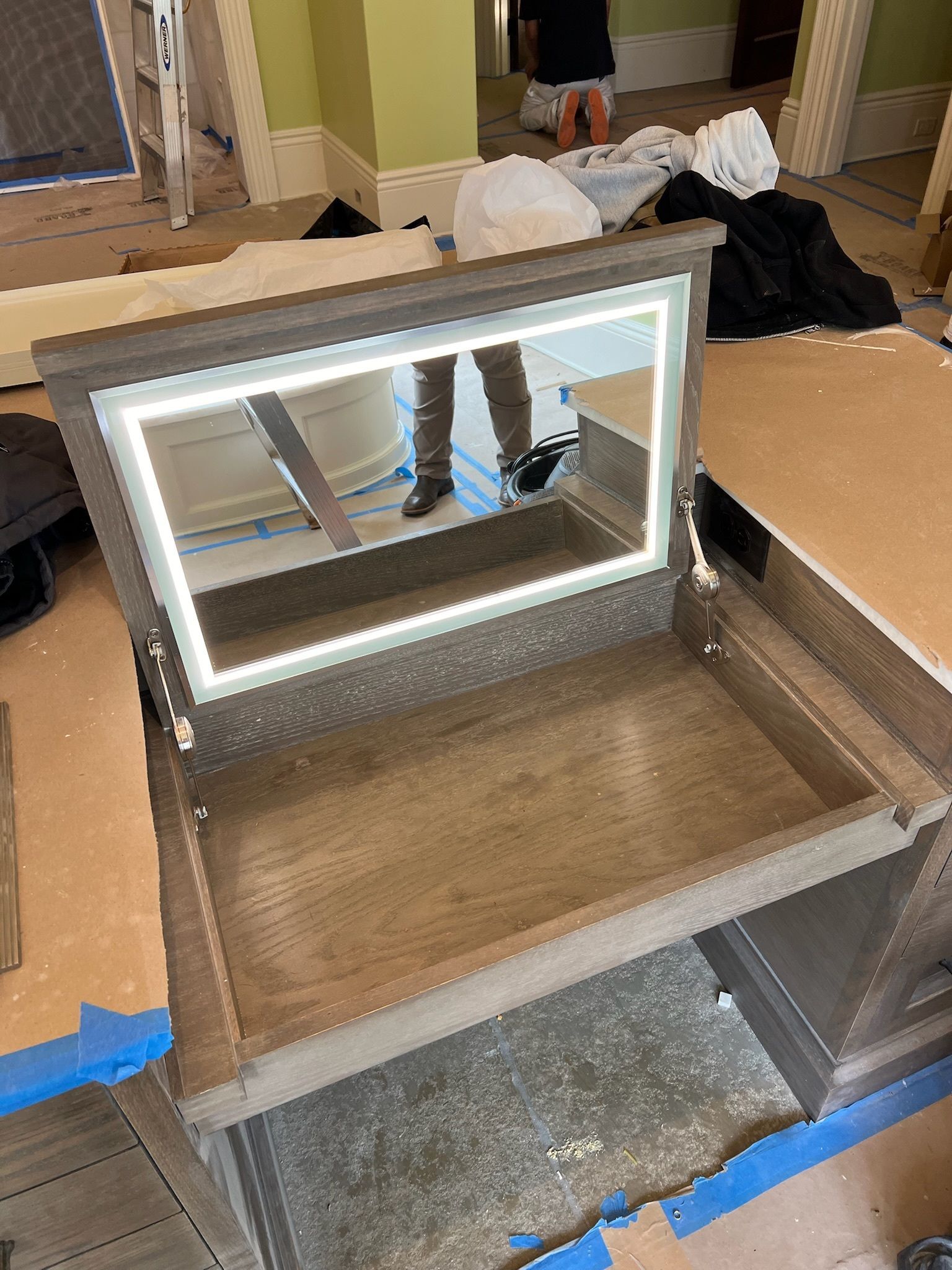 Open wooden drawer with a mirror on the lid in a room with packing materials and blue tape on the floor