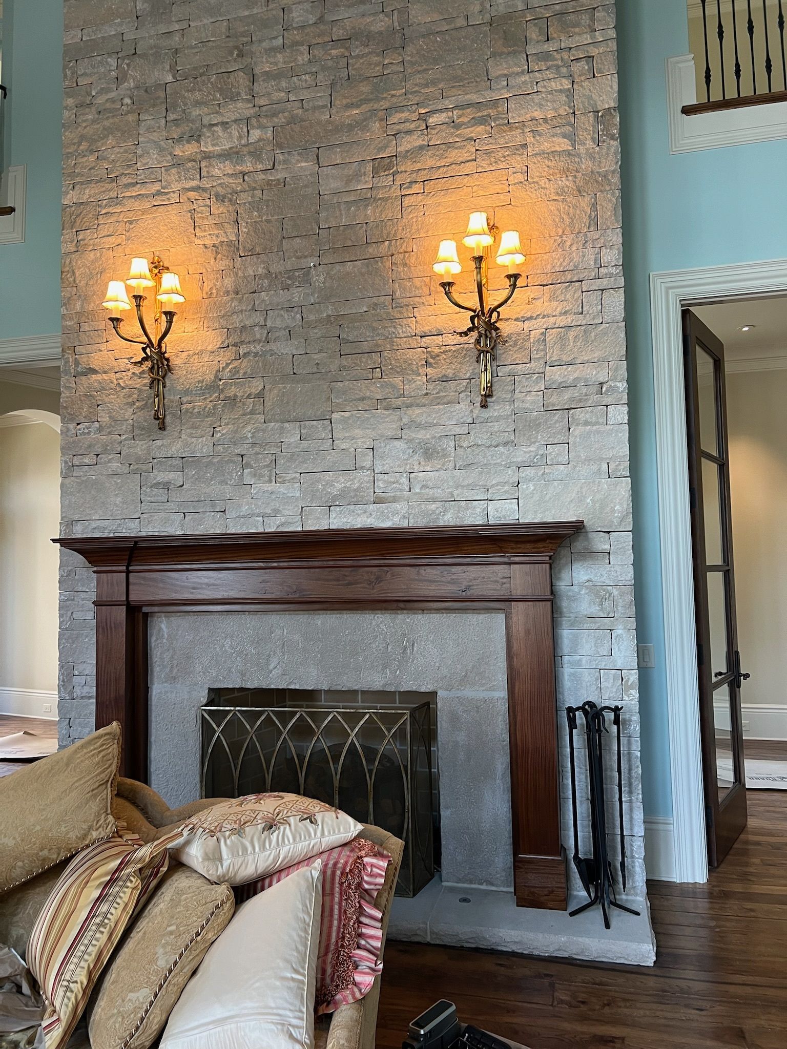 Elegant living room with stone fireplace, dark wood mantel, wall sconces, and light blue walls