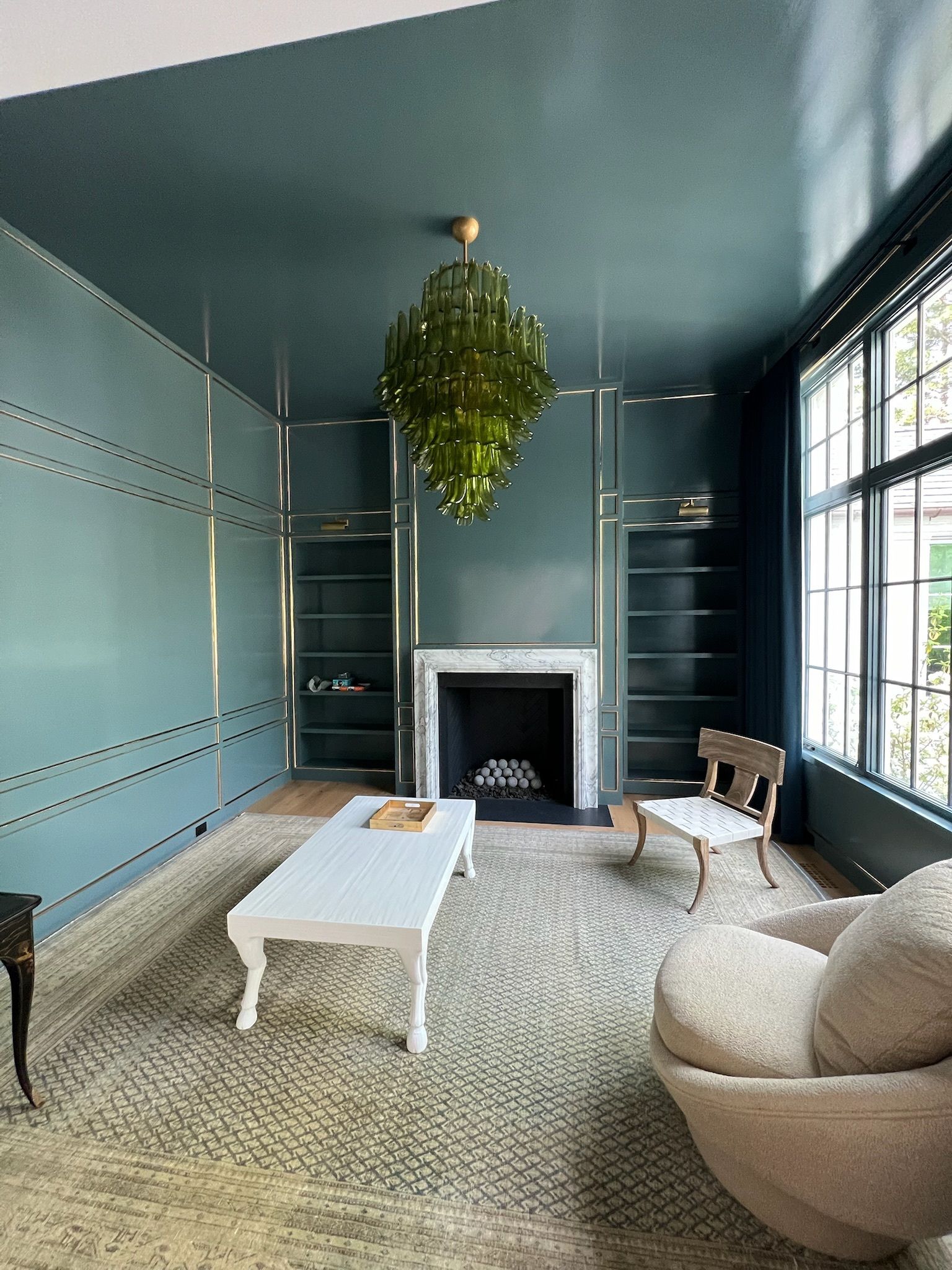 Blue living room with fireplace, large window, hanging plant, white rug, and modern chairs