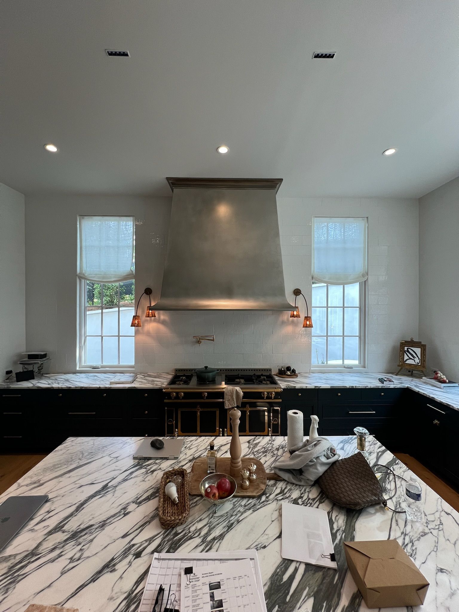 Modern kitchen with black cabinets, marble island, and large range hood beneath two windows