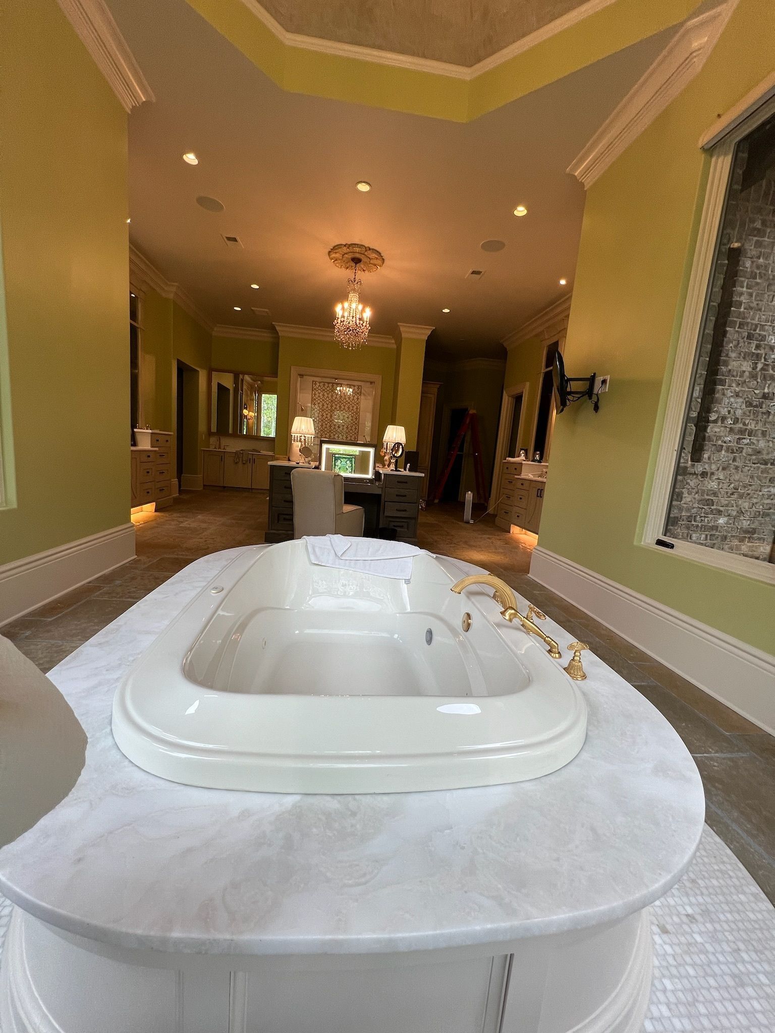 White jetted bathtub in a tiled bathroom with a chandelier and vanity in the background