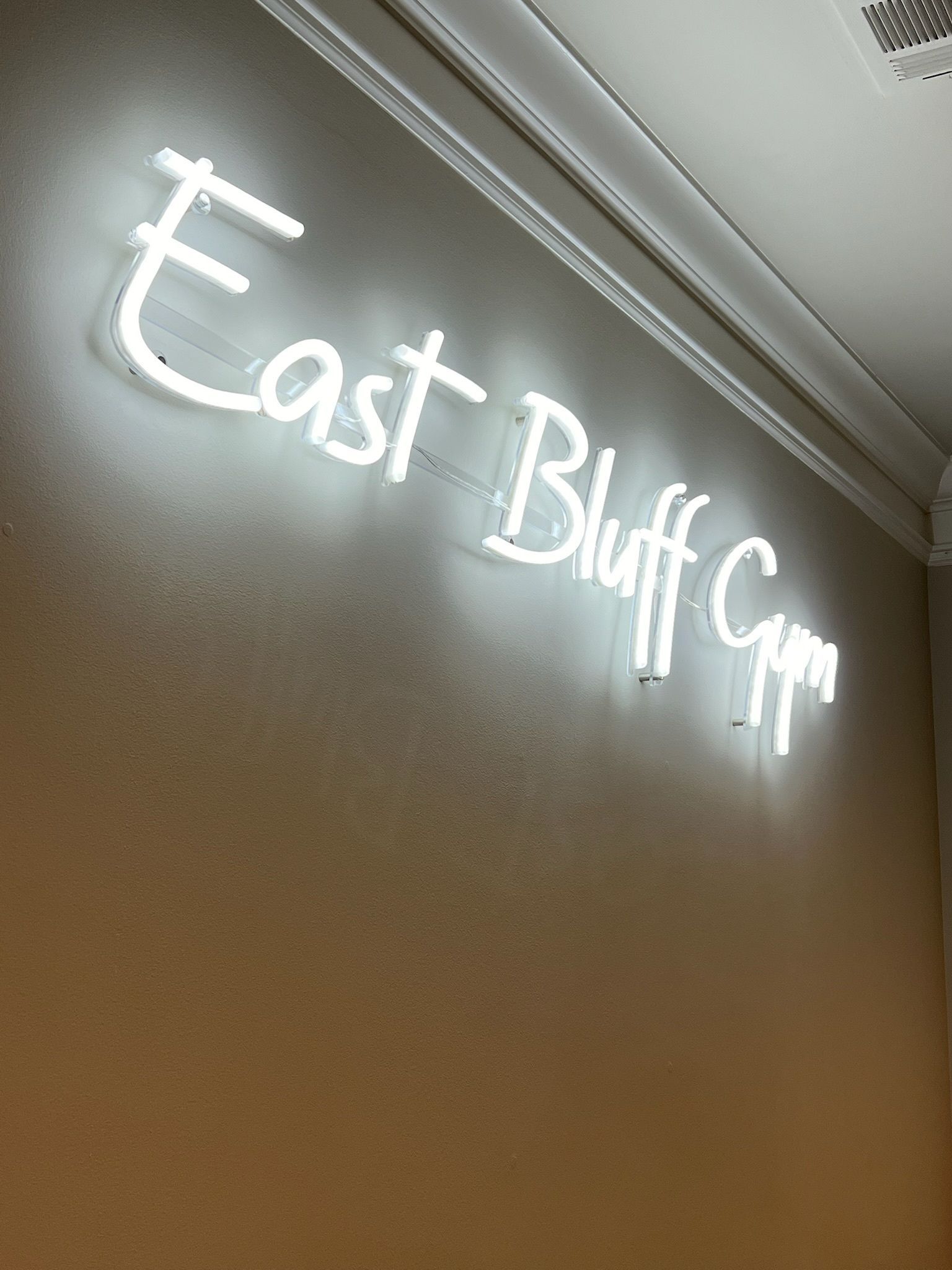Glowing white “East Bluff.com” sign on a tan wall near a ceiling trim
