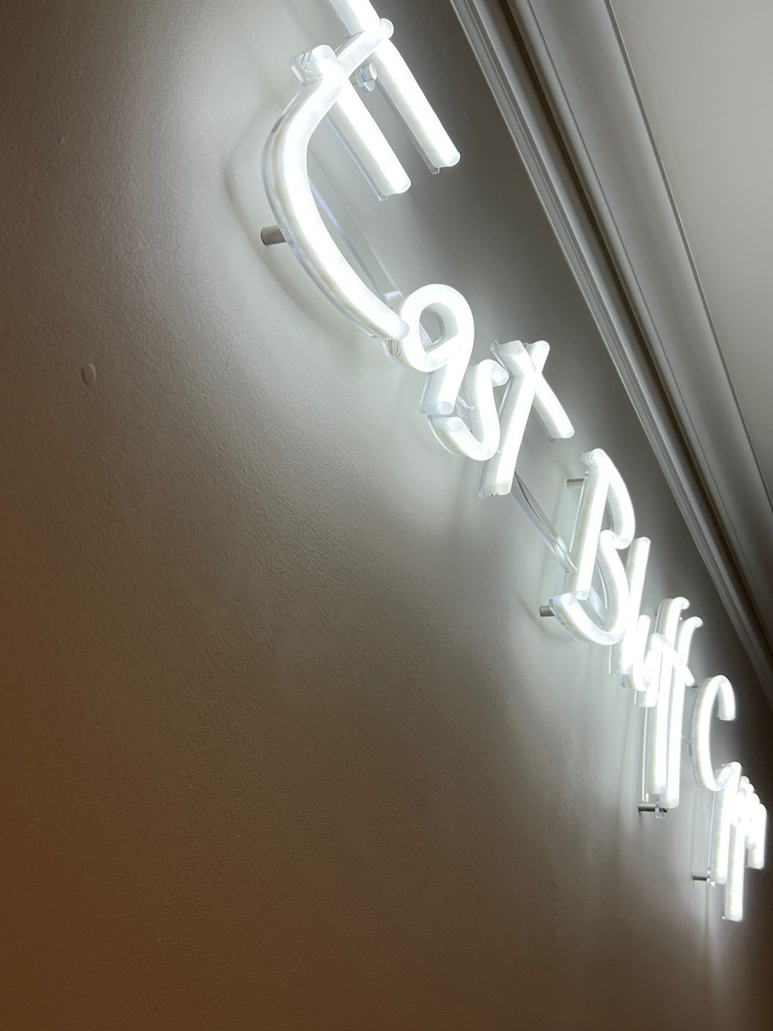 White neon “The Last Bank” sign on a wall, viewed at an angle.