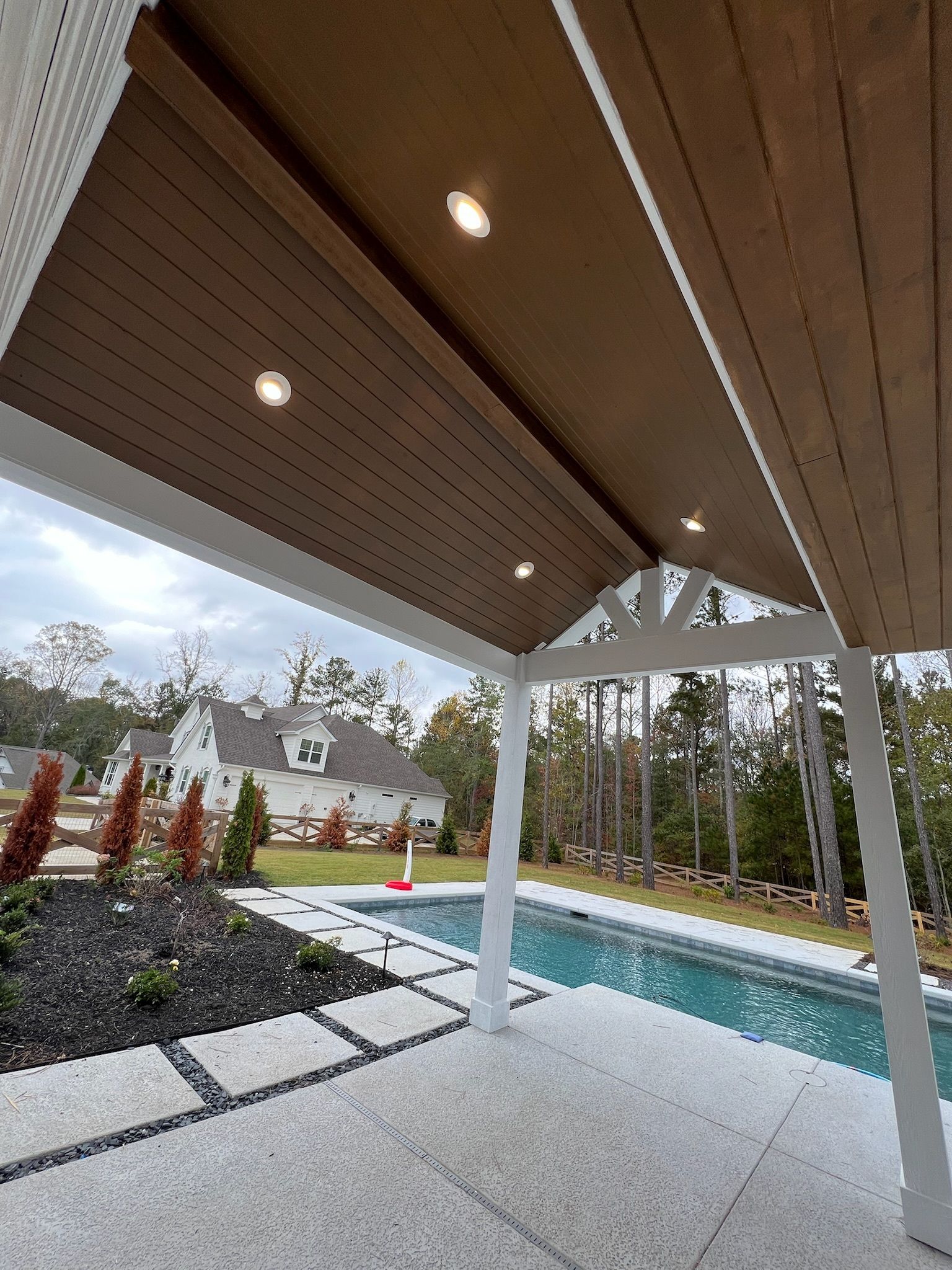 Covered patio overlooking backyard pool and landscaping with white posts and recessed lights