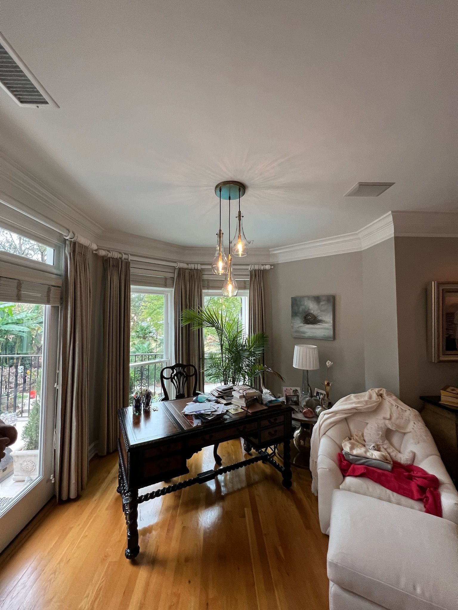 Bright dining room with a dark wooden table, chandelier, and large windows with curtains.