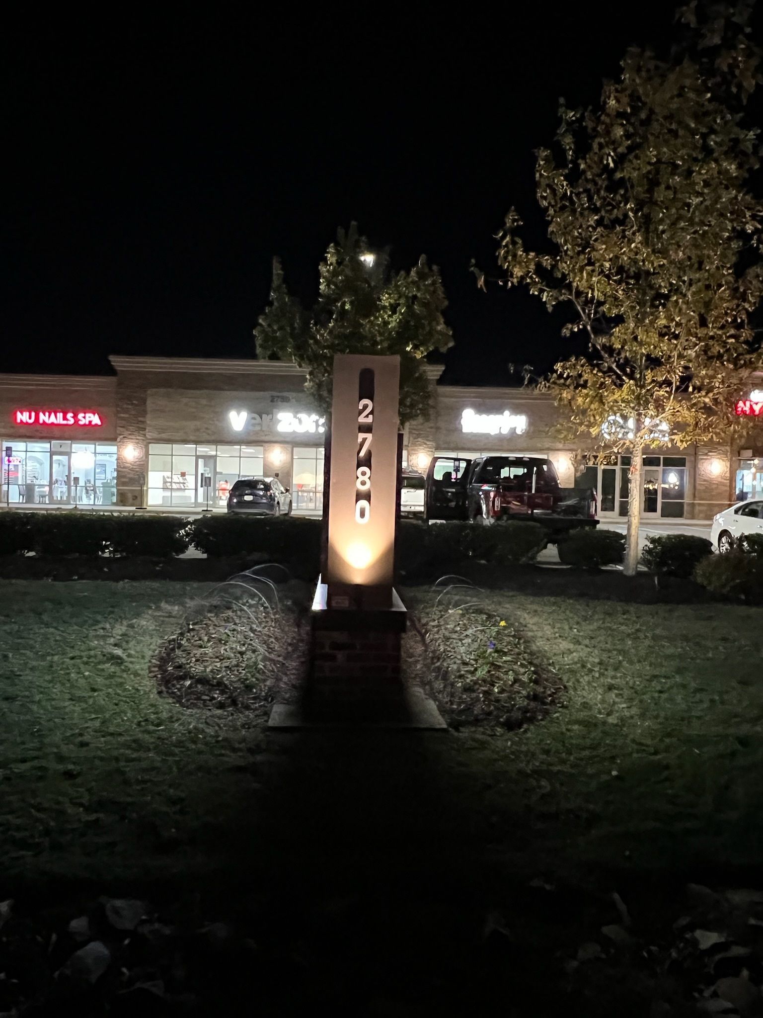 Nighttime shopping center with a lit monument sign and storefronts in the background