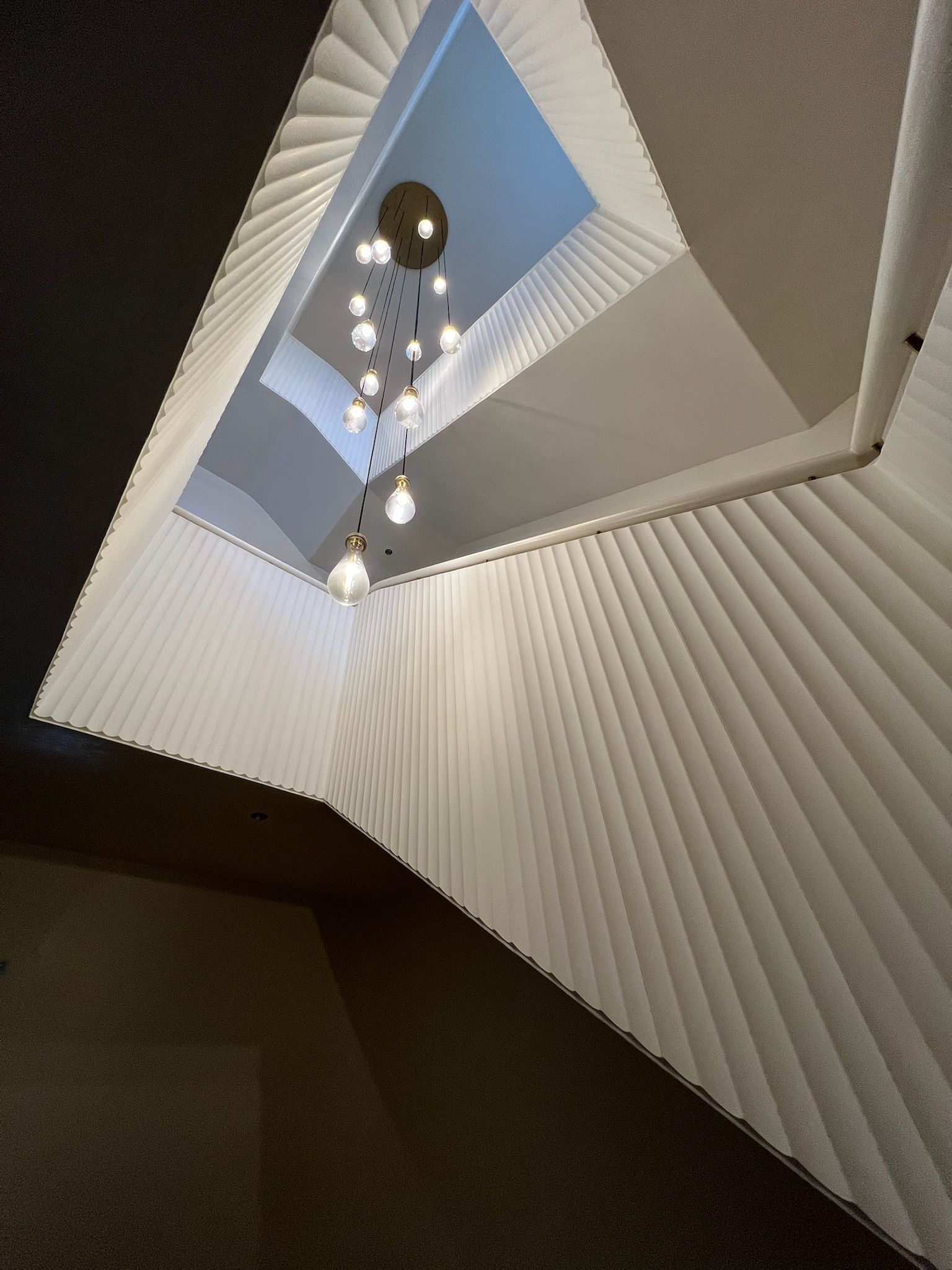 Spiral staircase looking up toward a skylight with hanging pendant lights.