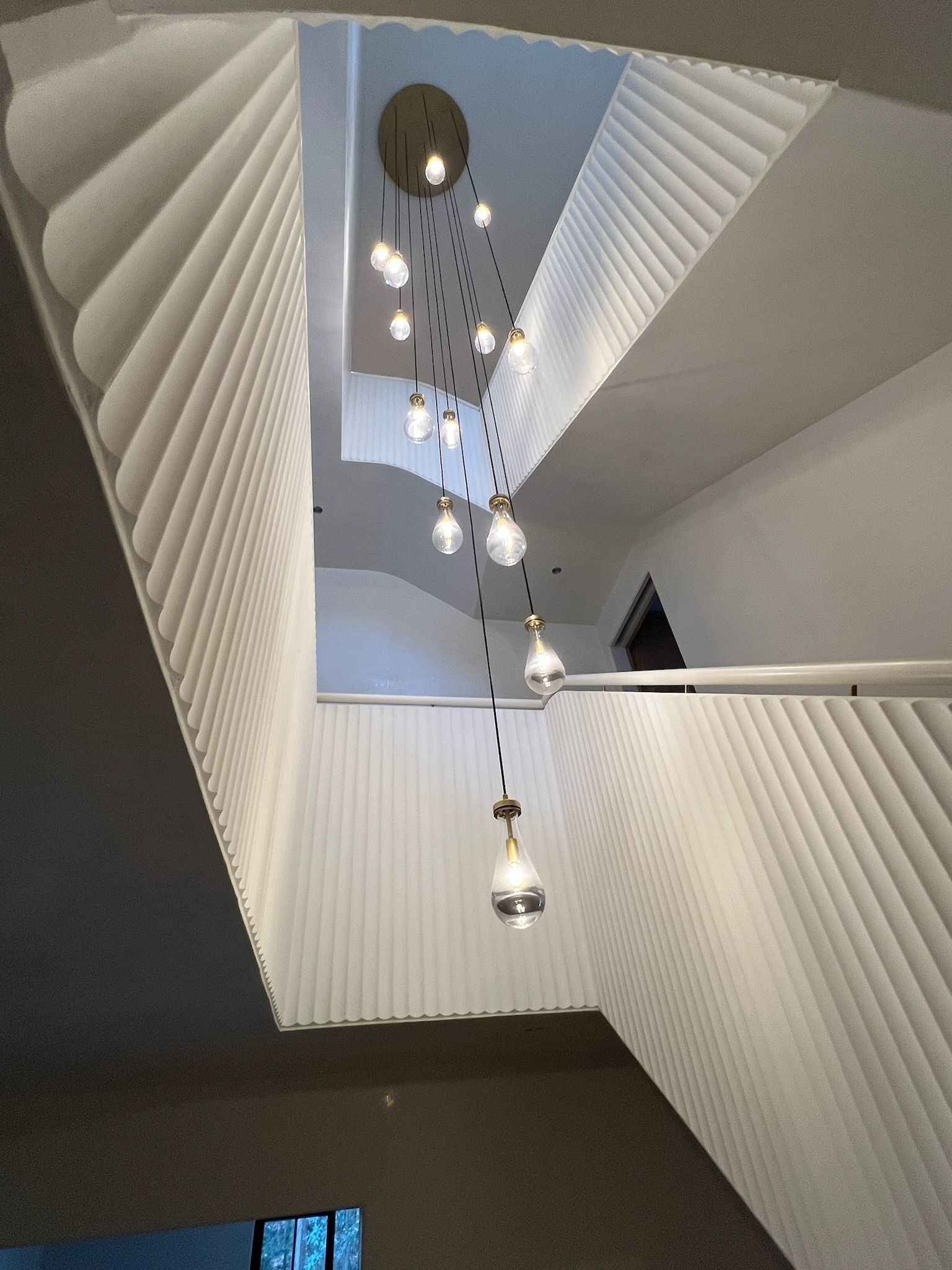 Modern spiral staircase with white railings and hanging pendant lights in a bright interior.