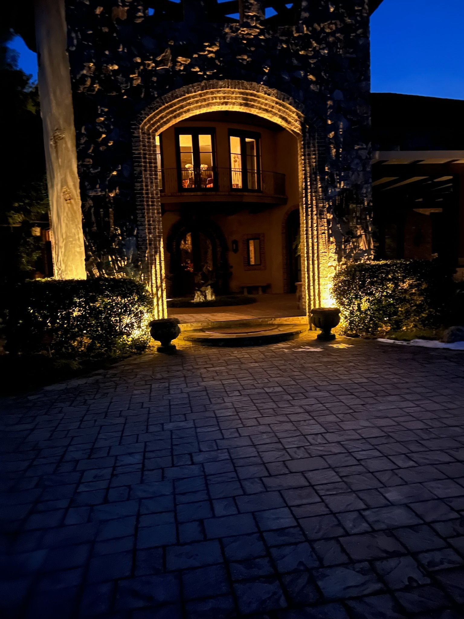 Brick house entrance lit by warm lights at night, with a glowing arched doorway and paved courtyard