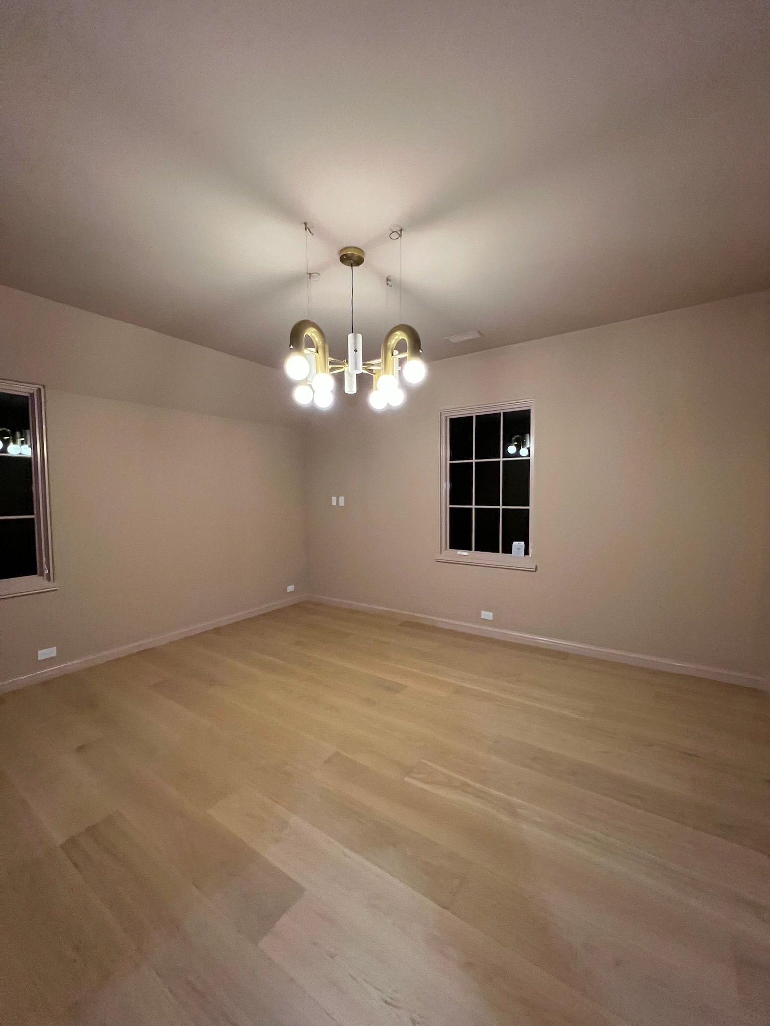 Empty beige room with hardwood floor, two windows, and a chandelier ceiling light