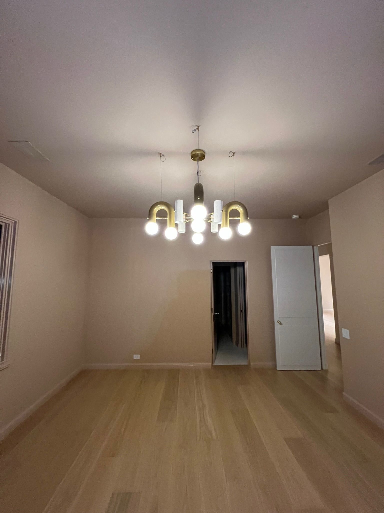 Empty beige room with wood floor and a brass chandelier hanging from the ceiling