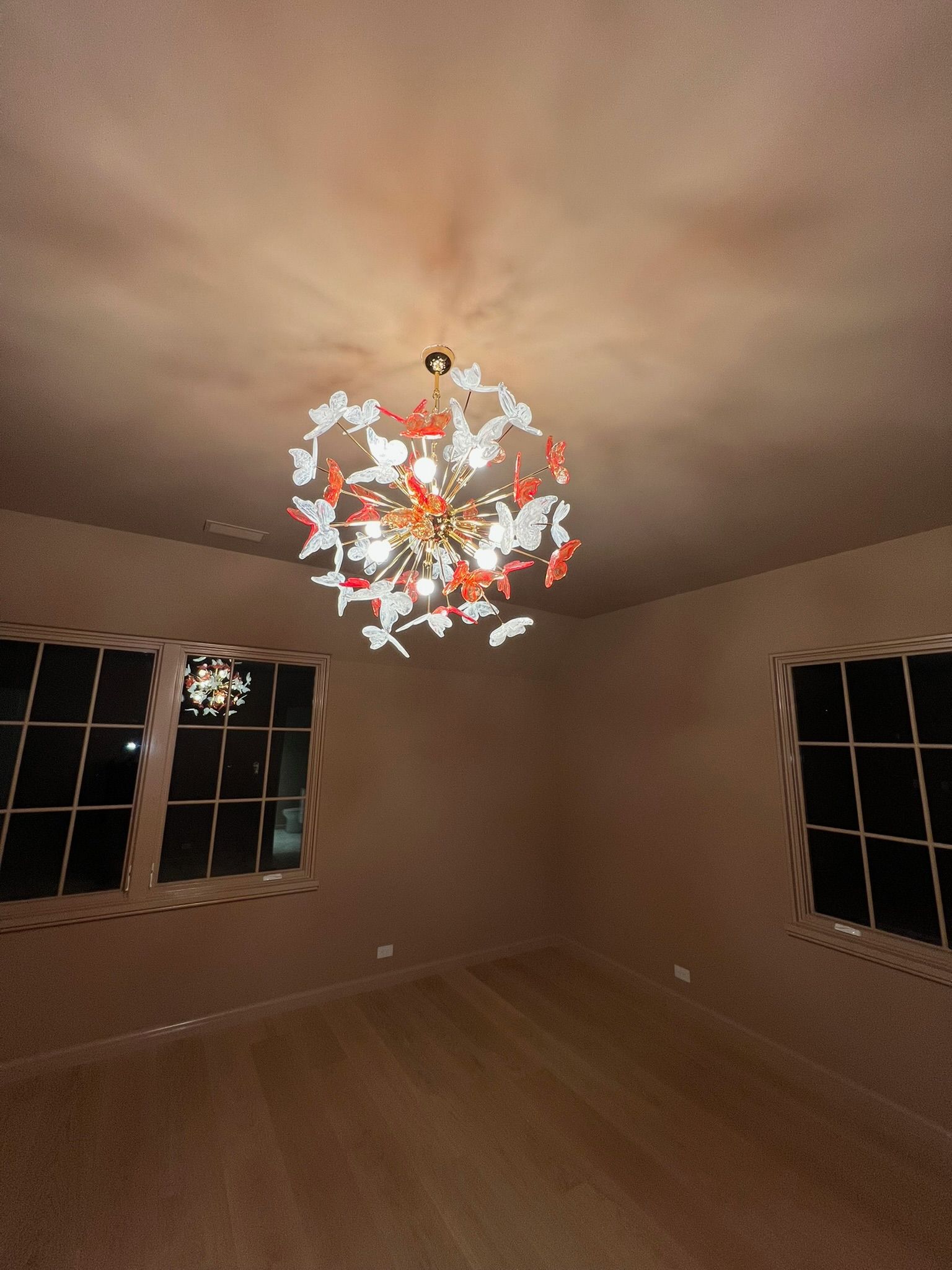 Empty room with beige walls, dark windows, and a colorful ceiling light fixture.