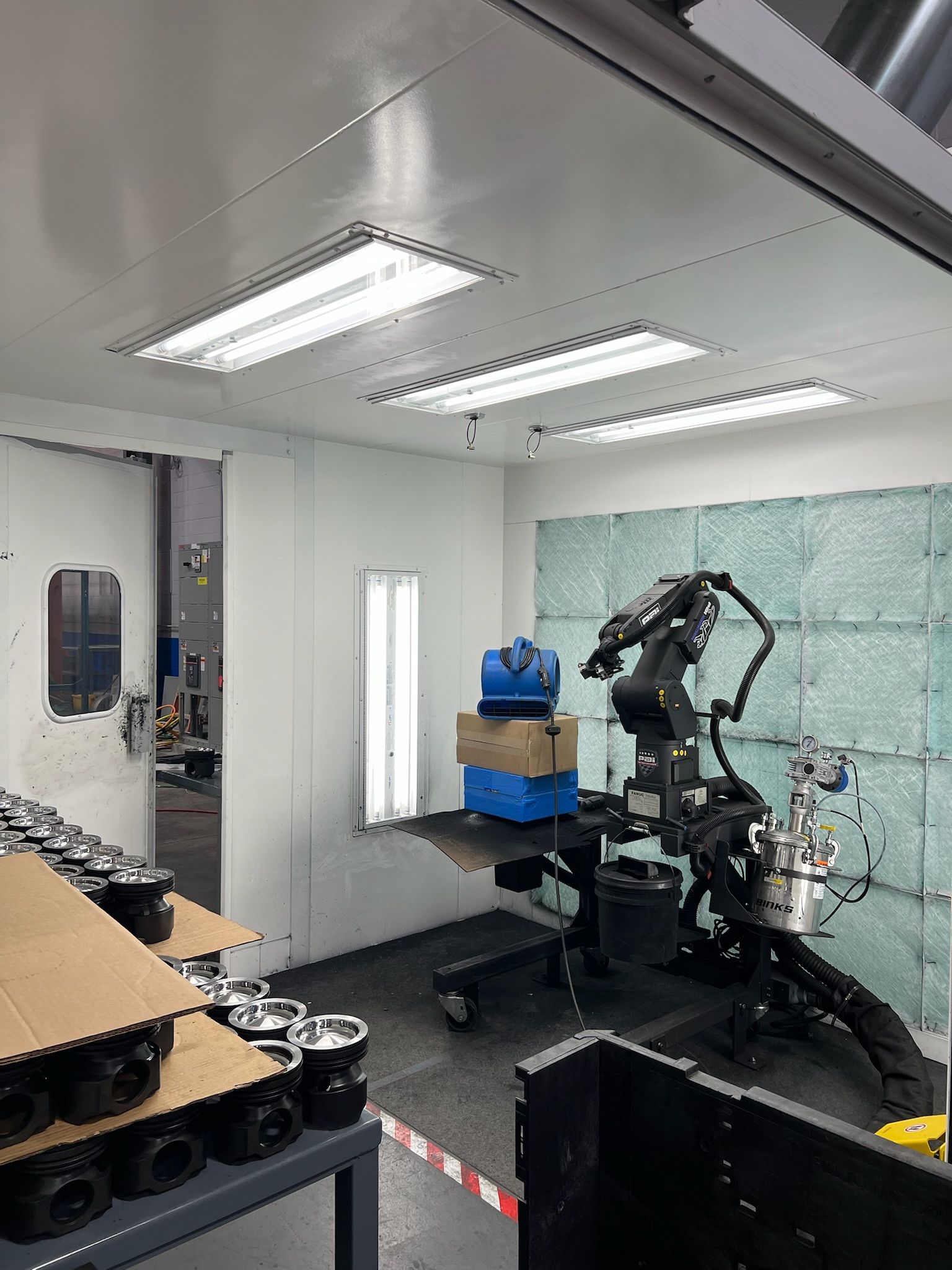 Robot arm in a small industrial lab with workbenches, tools, and bright overhead lights