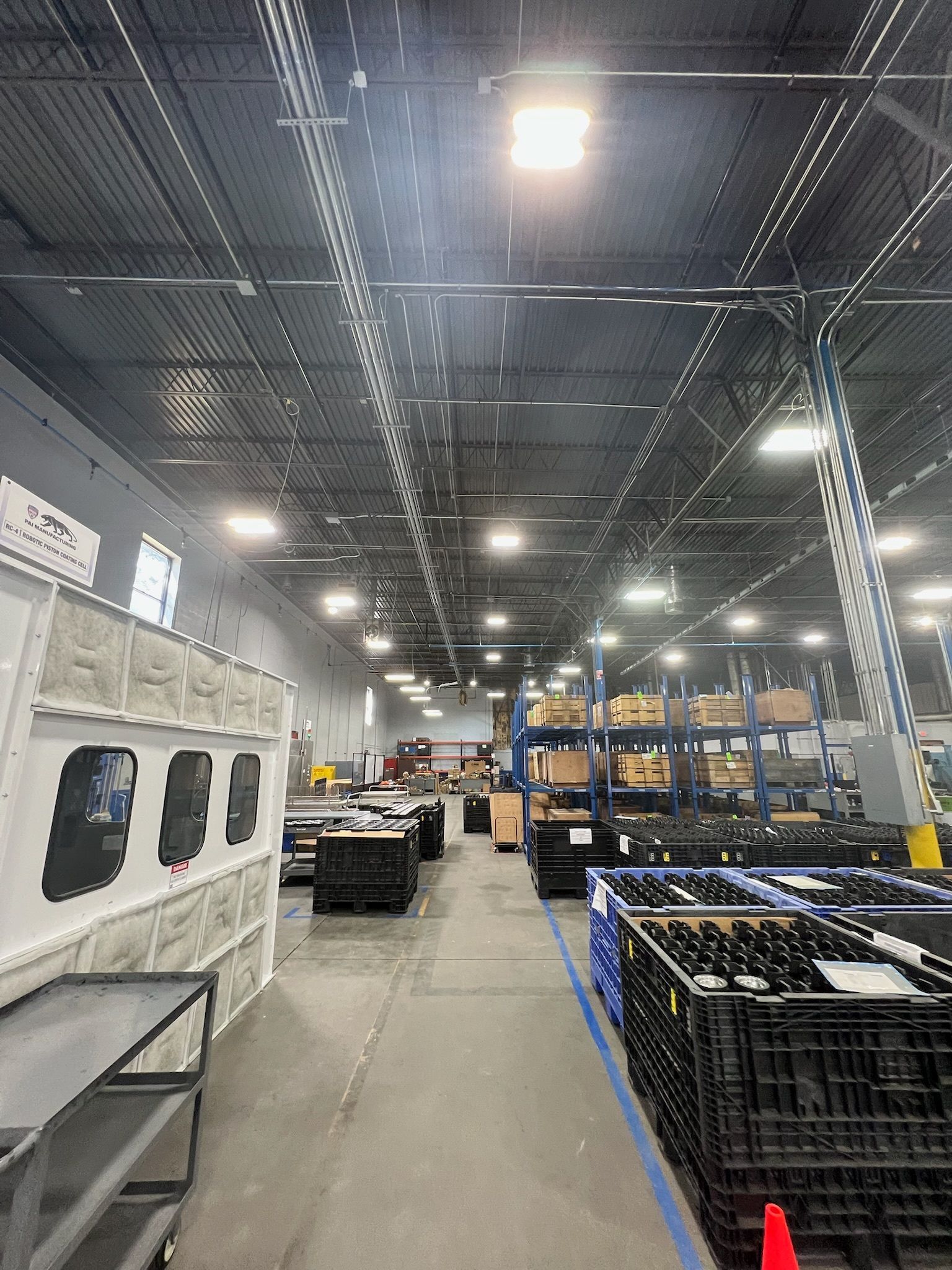 Warehouse aisle with stacked bins, shelving, and overhead lights in an industrial interior