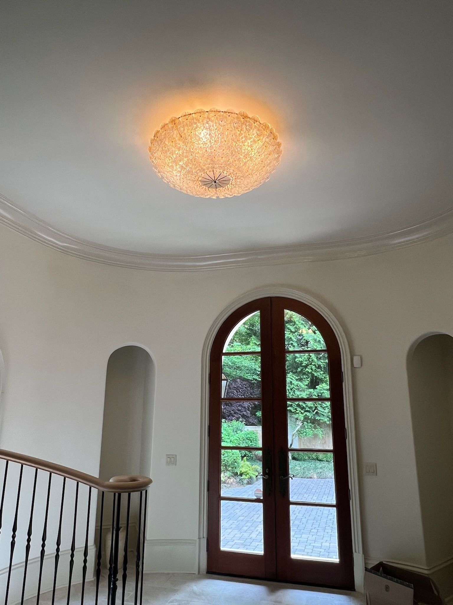 Bright entryway with arched wooden glass doors, curved stairs, and a glowing ceiling light