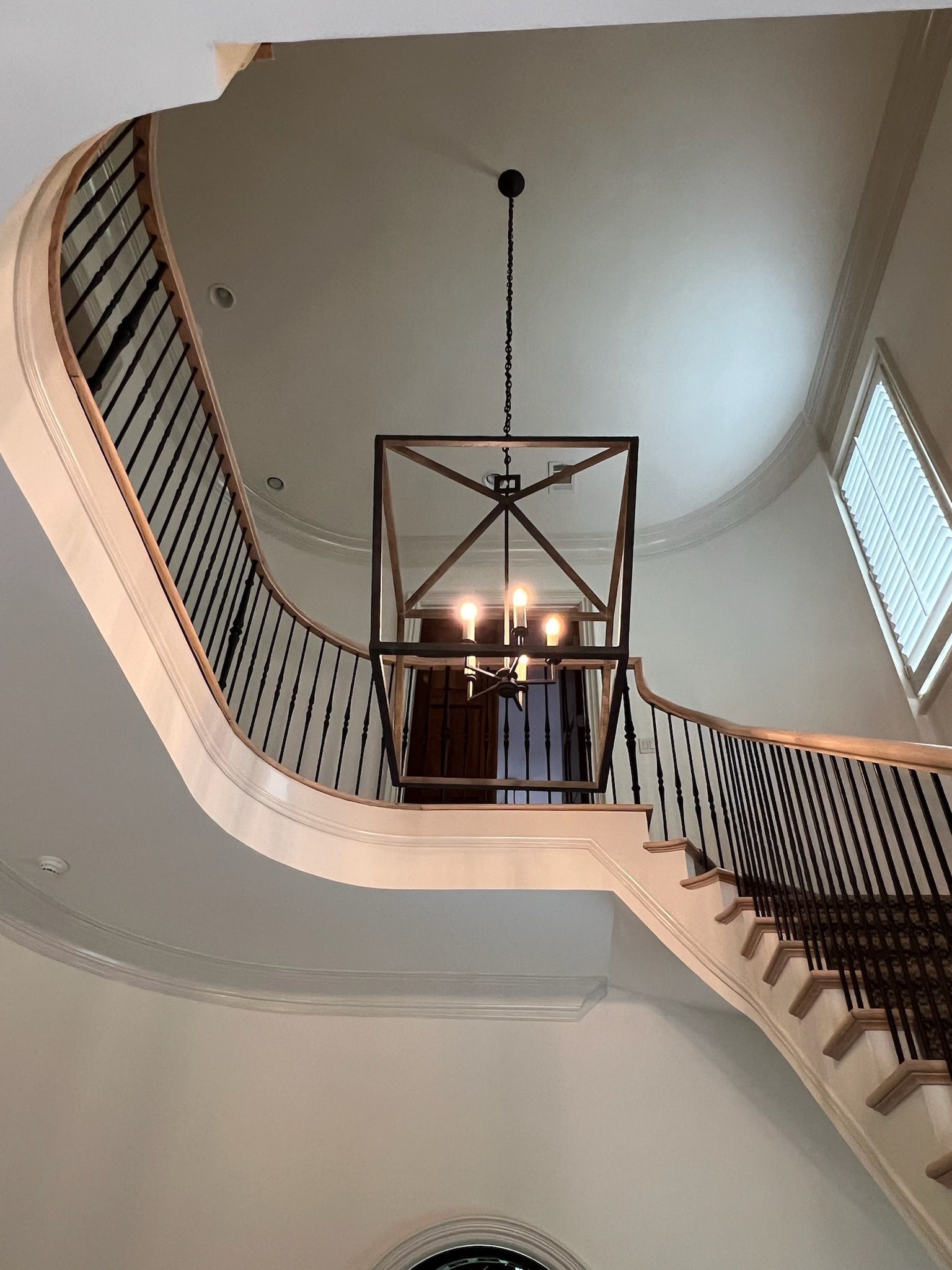 Curved staircase with black railings and chandelier in a bright interior foyer
