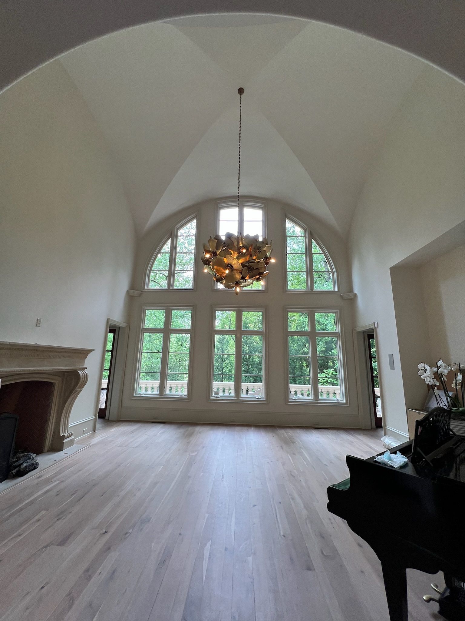 Elegant living room with vaulted ceiling, large arched windows, chandelier, and fireplace