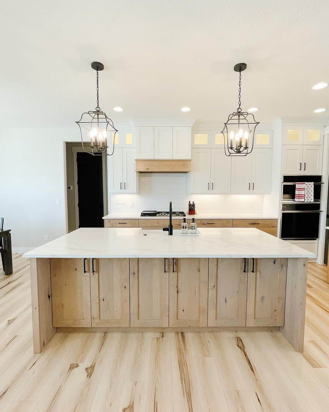 Bright modern kitchen with white cabinets, large island, pendant lights, and light wood floors