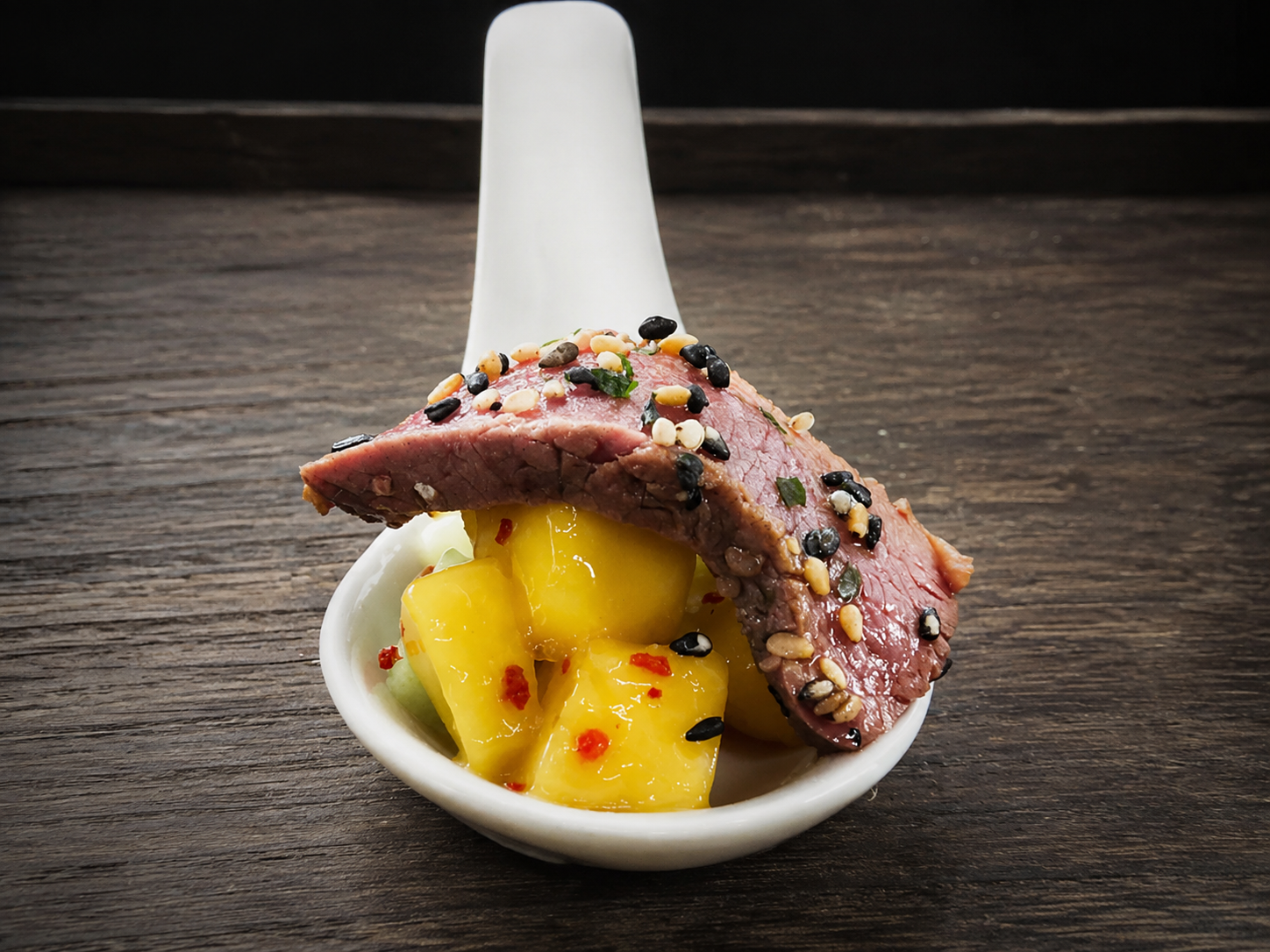Rosé hertenzadel met mango-komkommersalade geserveerd op een porseleinen amuselepel