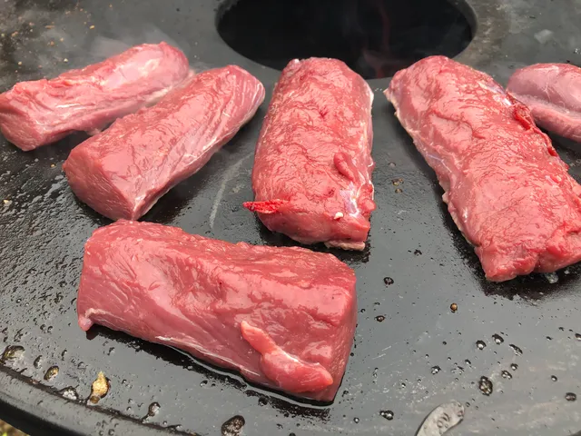 Stukken hertenzadel worden rondom aangebakken op een hete plancha