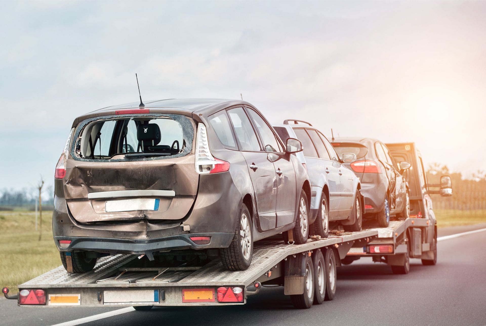 Damaged car on a tow truck, traveling on a highway. Other vehicles are also being transported.