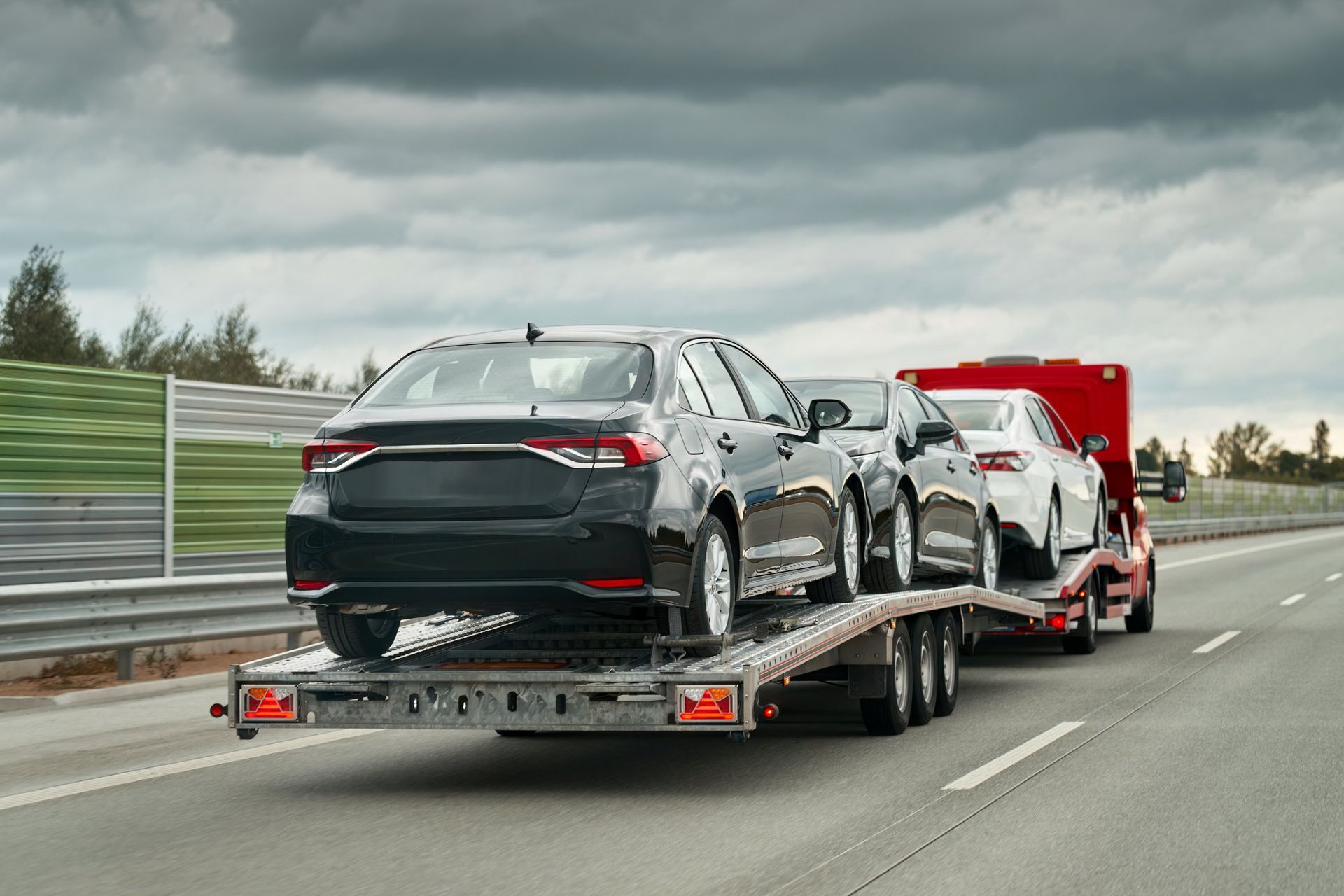 Car carrier trailer transporting new cars on a highway under a cloudy sky.