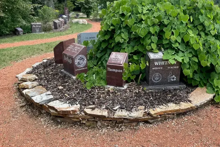 Memorial garden with engraved stone markers and leafy green shrub on a red gravel path