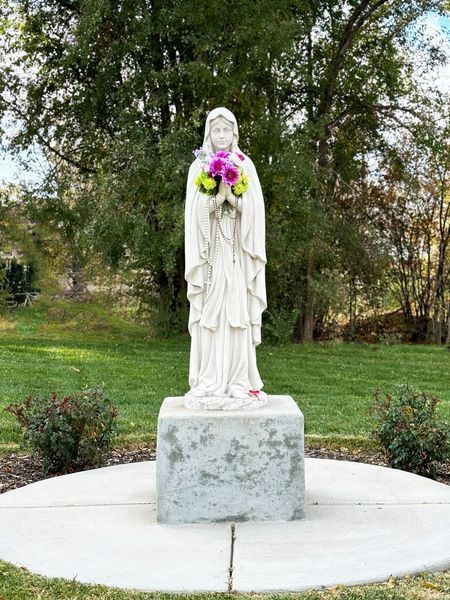 Memorial wall with plaques, white statue, and colorful flower beds under a bright blue sky