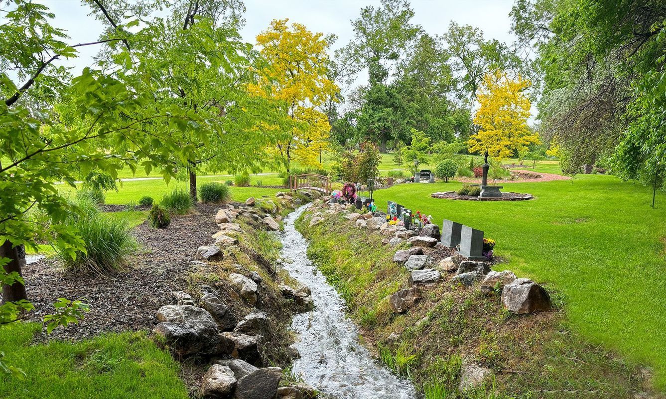 Landscaped park with a narrow stream, rocks, green trees, and people sitting on benches