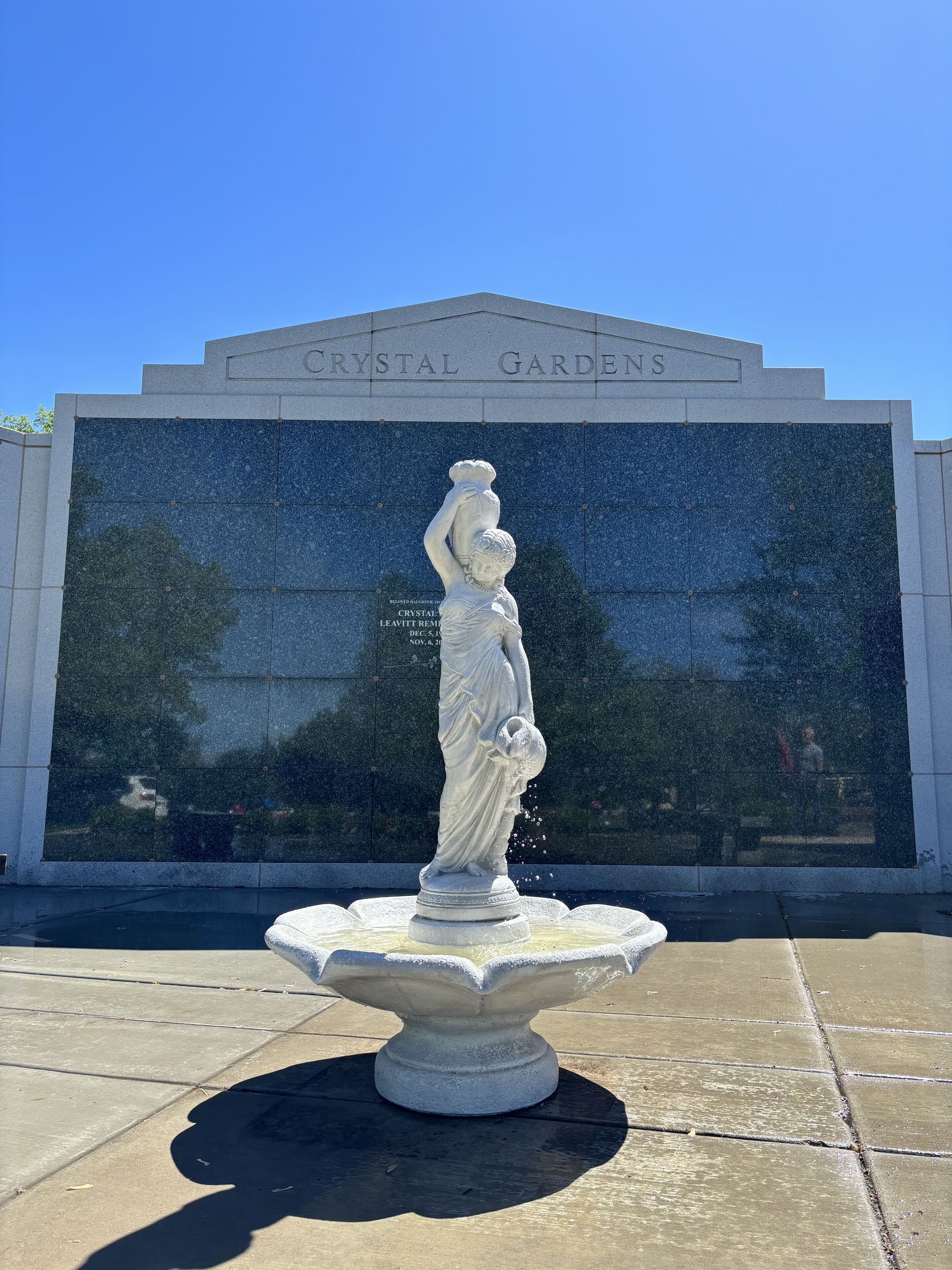 White stone fountain in front of a mausoleum with dark glass doors under a clear blue sky