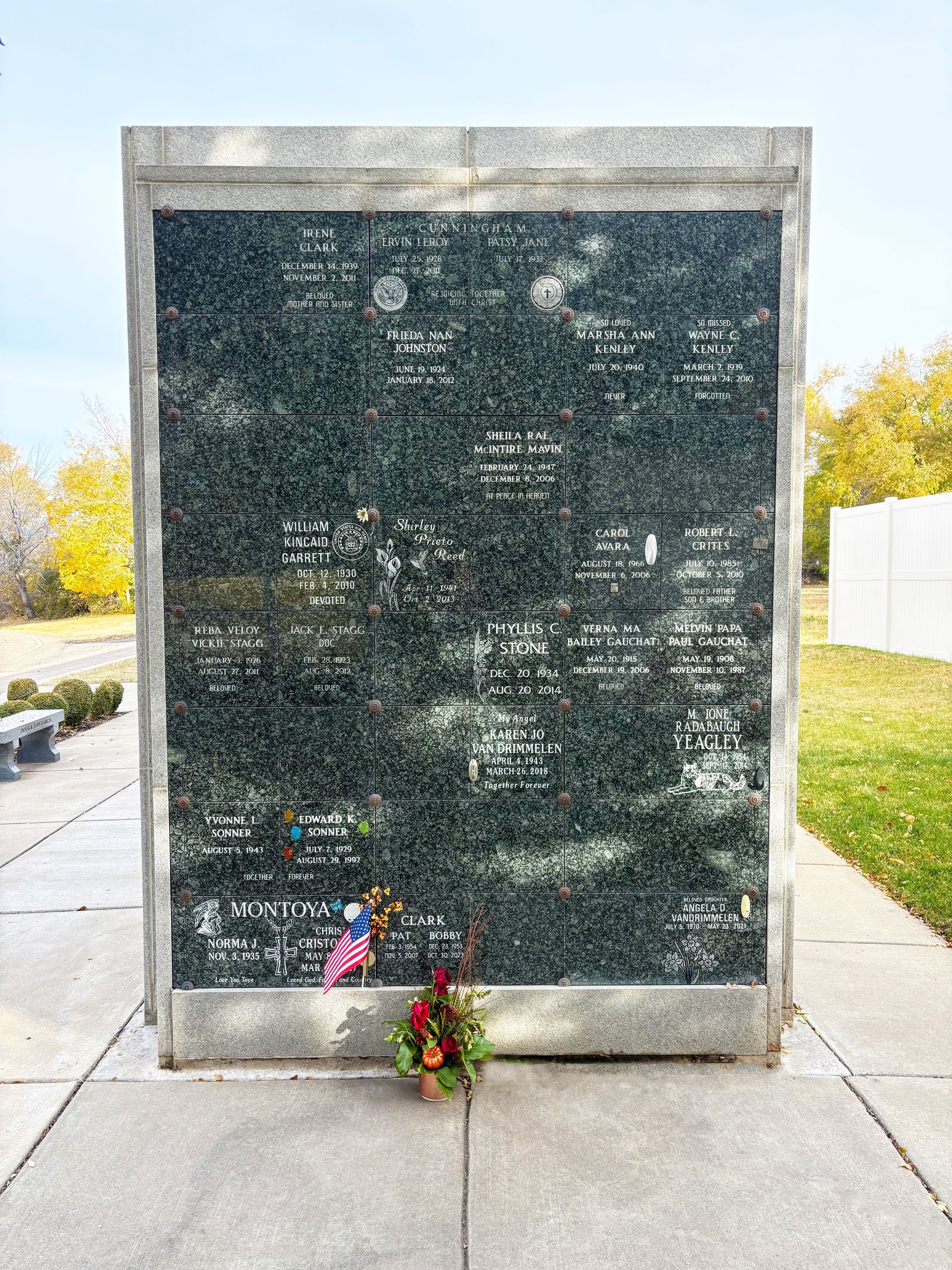 Dark memorial plaque with engraved text and flowers at the base outdoors